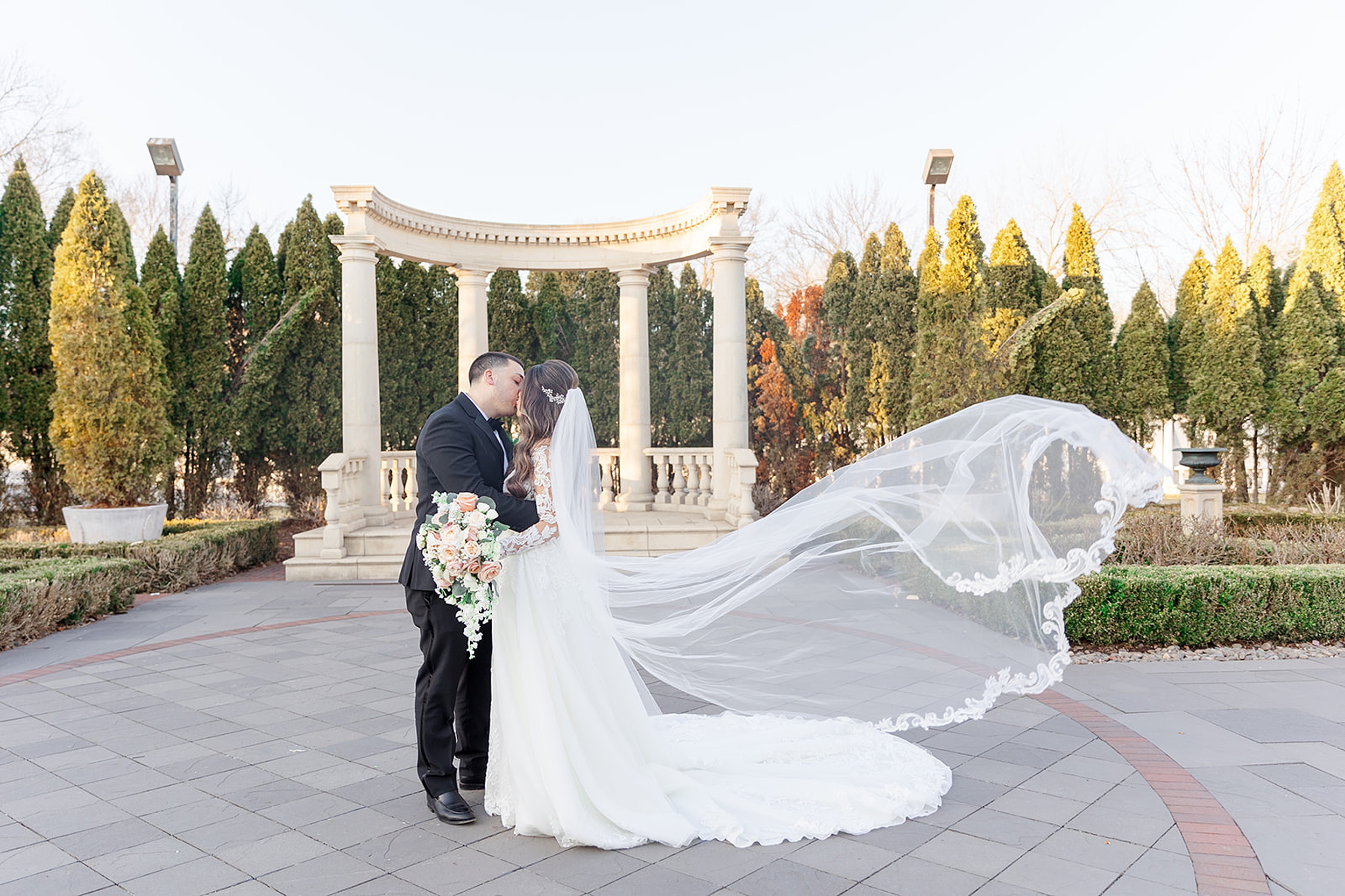 Newlyweds kiss in a garden patio while the veil flies in the wind at the rockleigh wedding venue