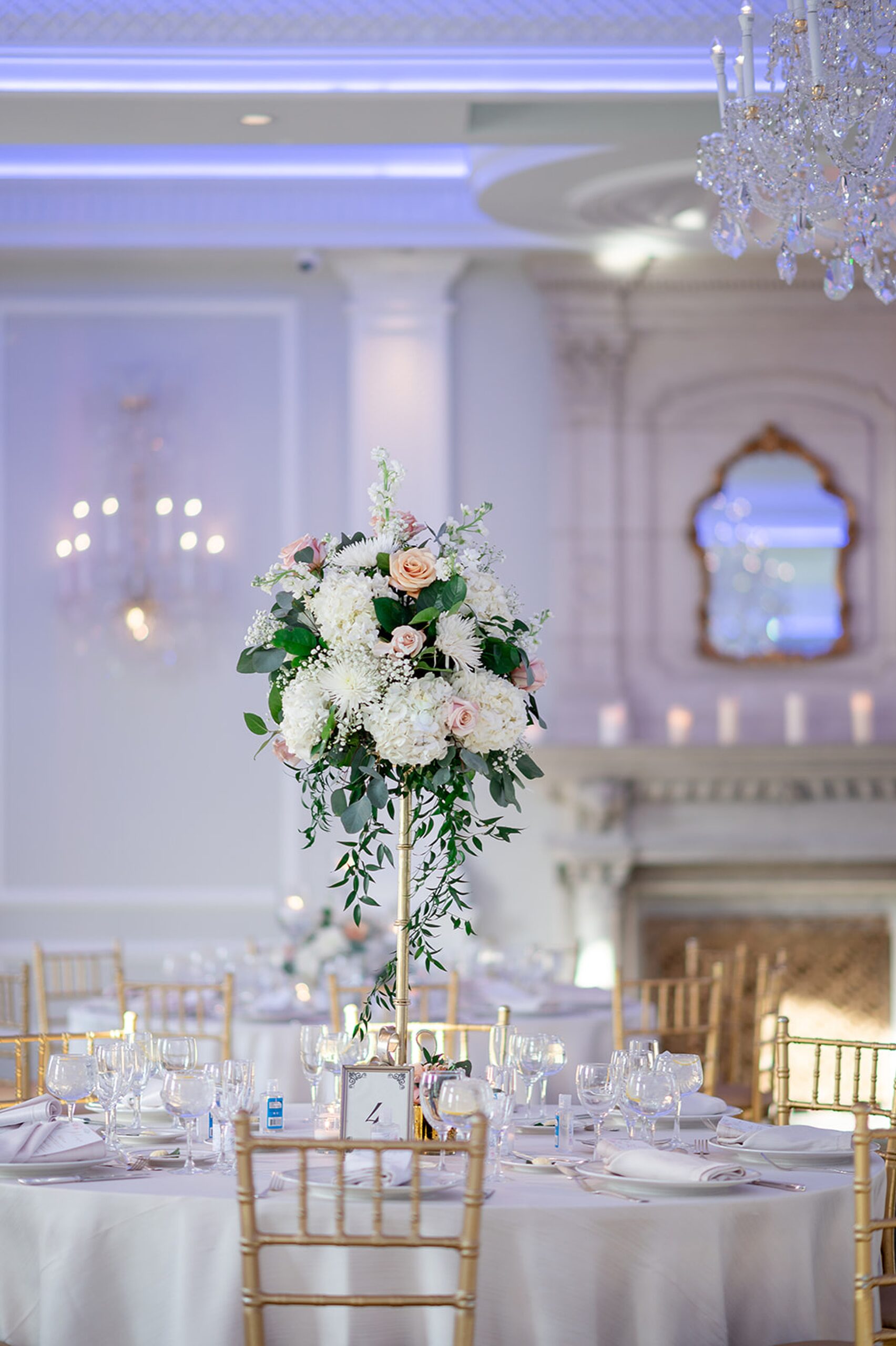 Details of a wedding reception table with a tall floral centerpiece and gold chairs