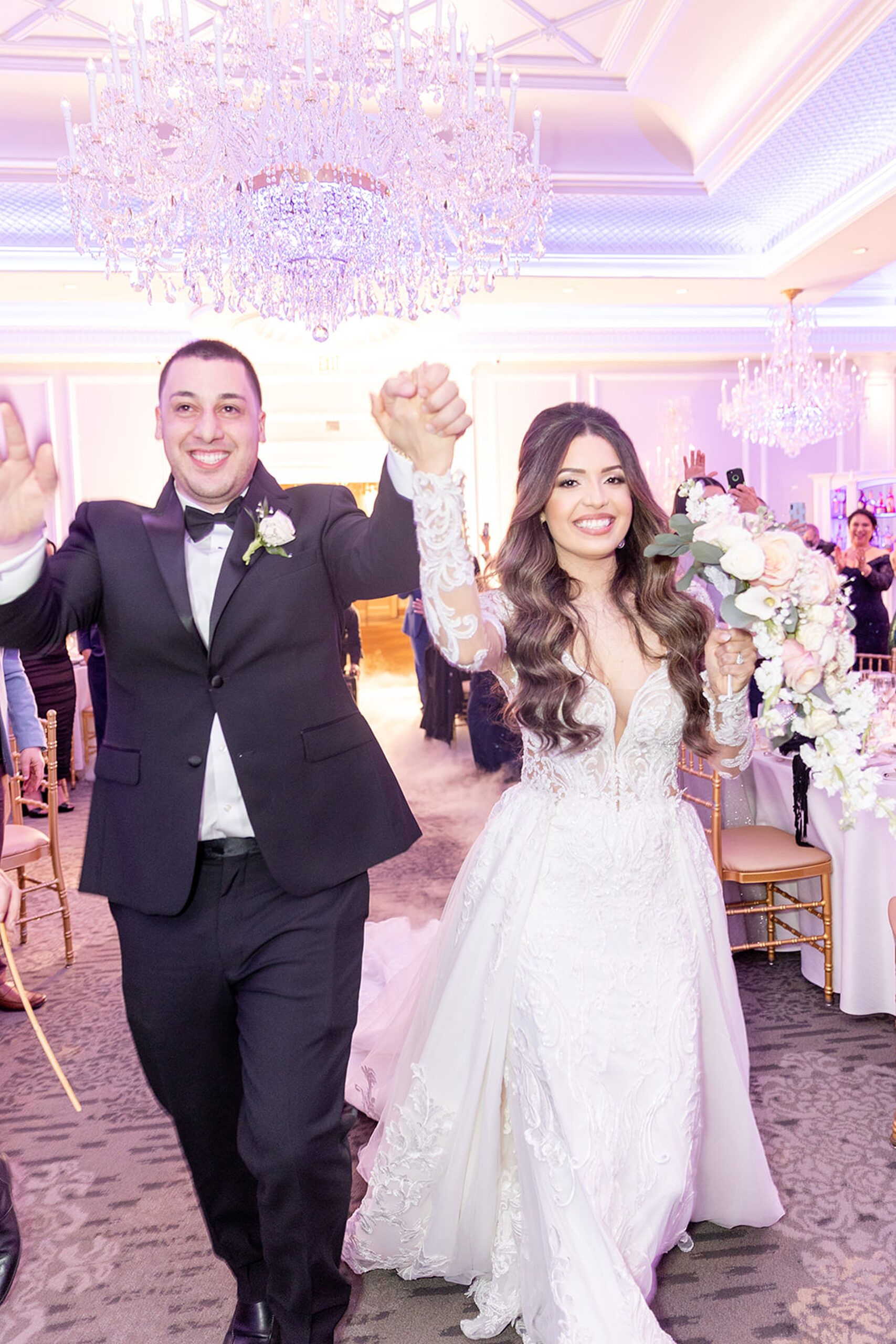 Newlyweds enter their wedding receptions with large crystal chandeliers