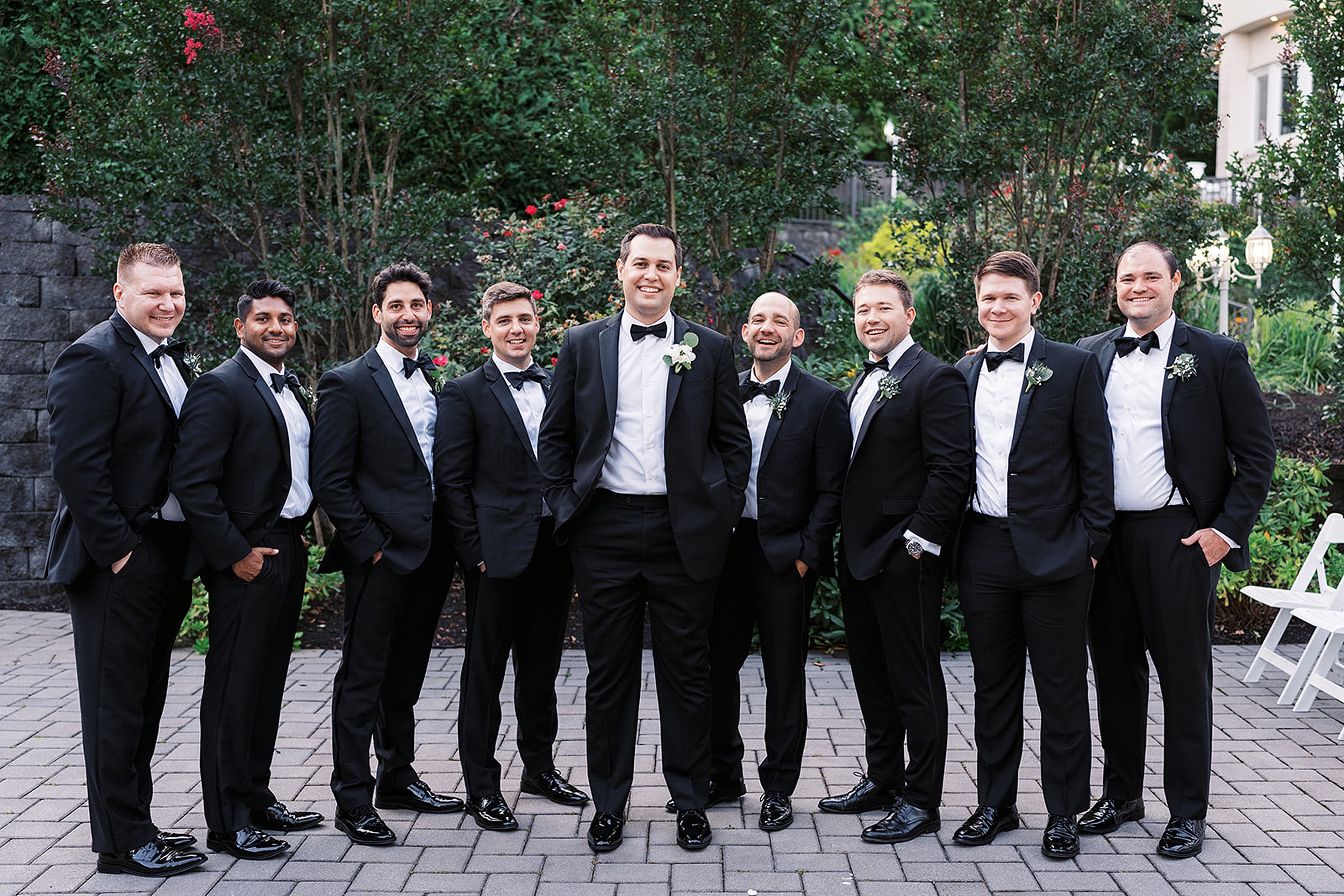A groom stands in a garden patio surrounded by his groomsmen all in black tuxedos