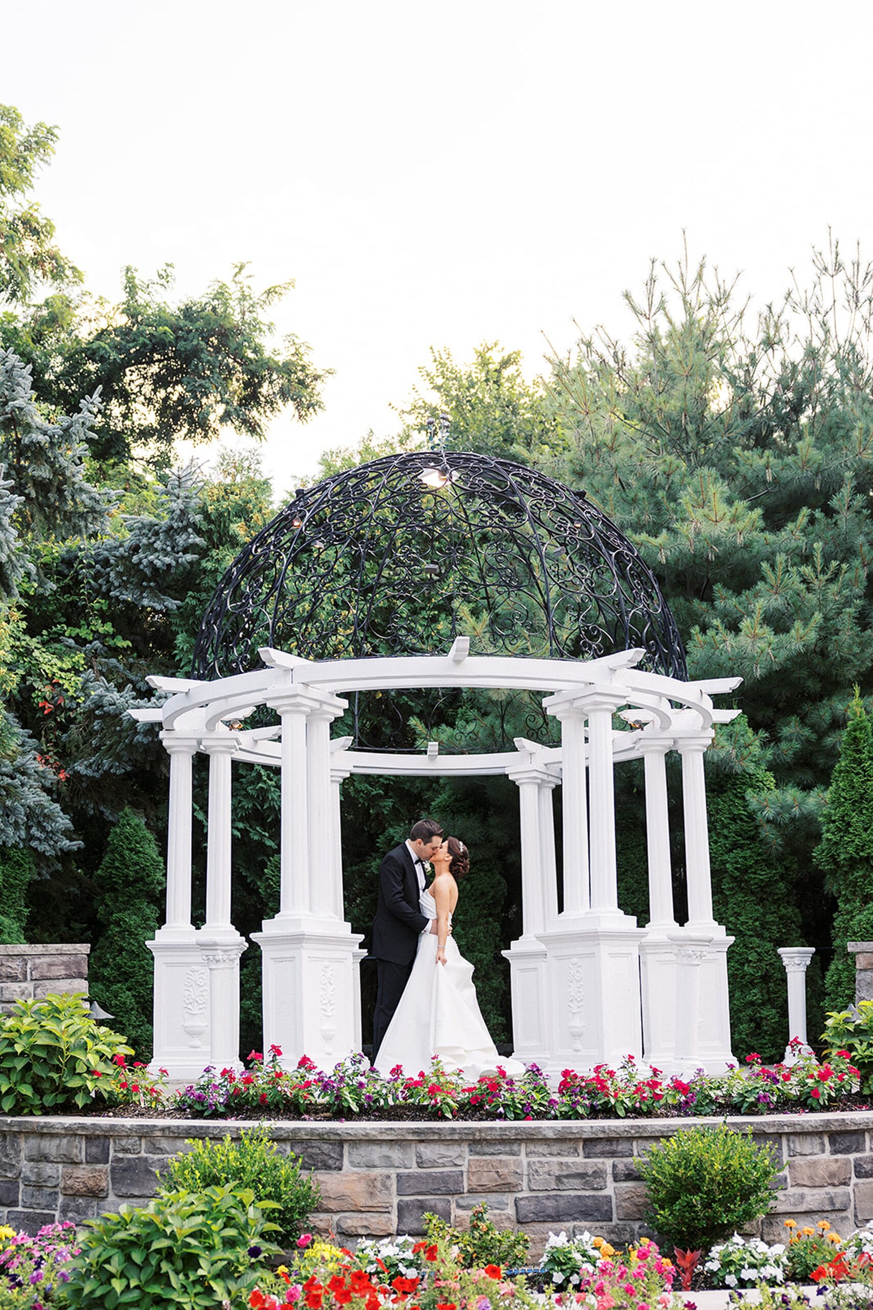 Newlyweds kiss under a large white gazebo in a garden at a valley regency wedding