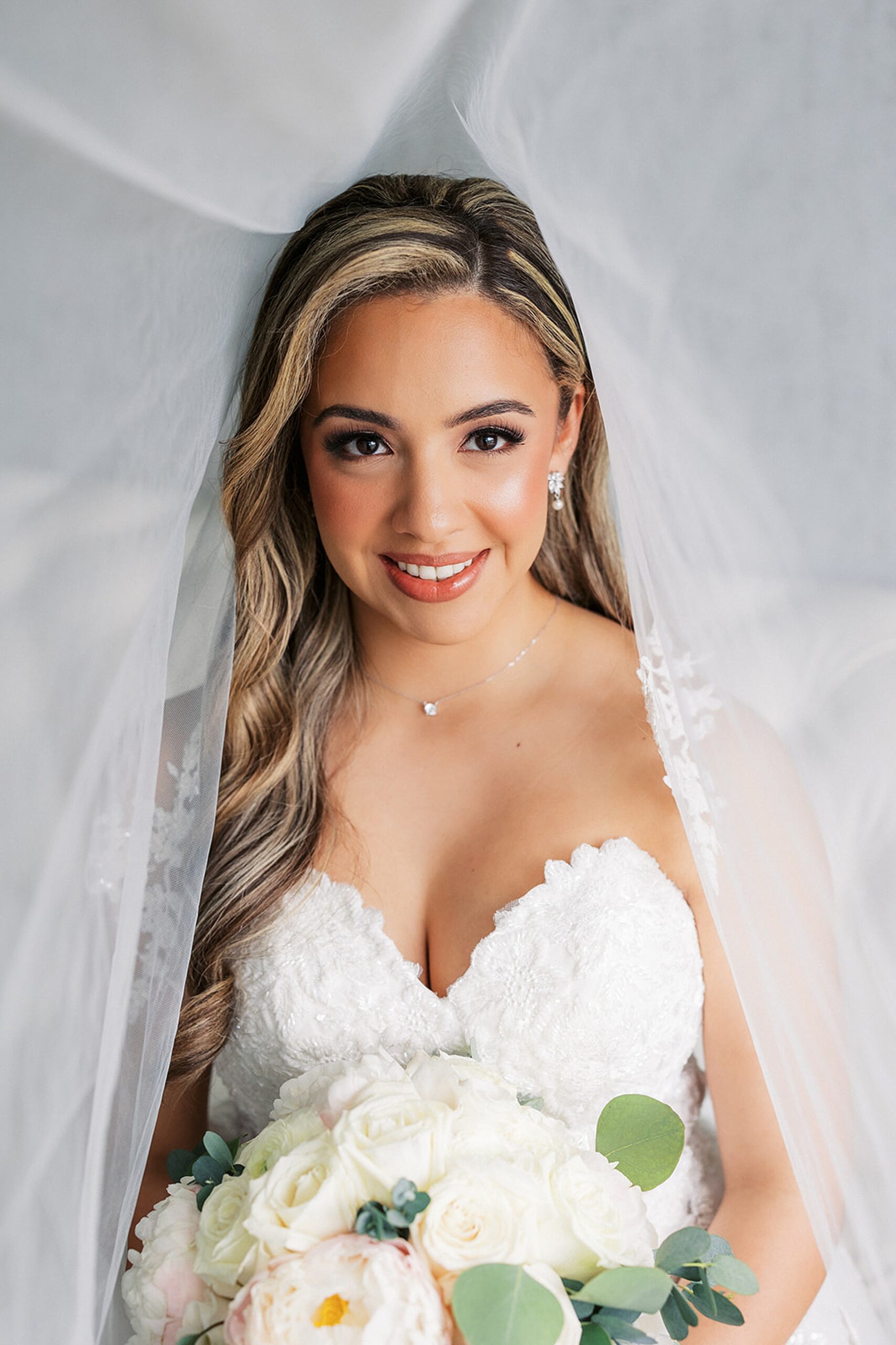 A bride hides under her veil while holding her white rose bouquet