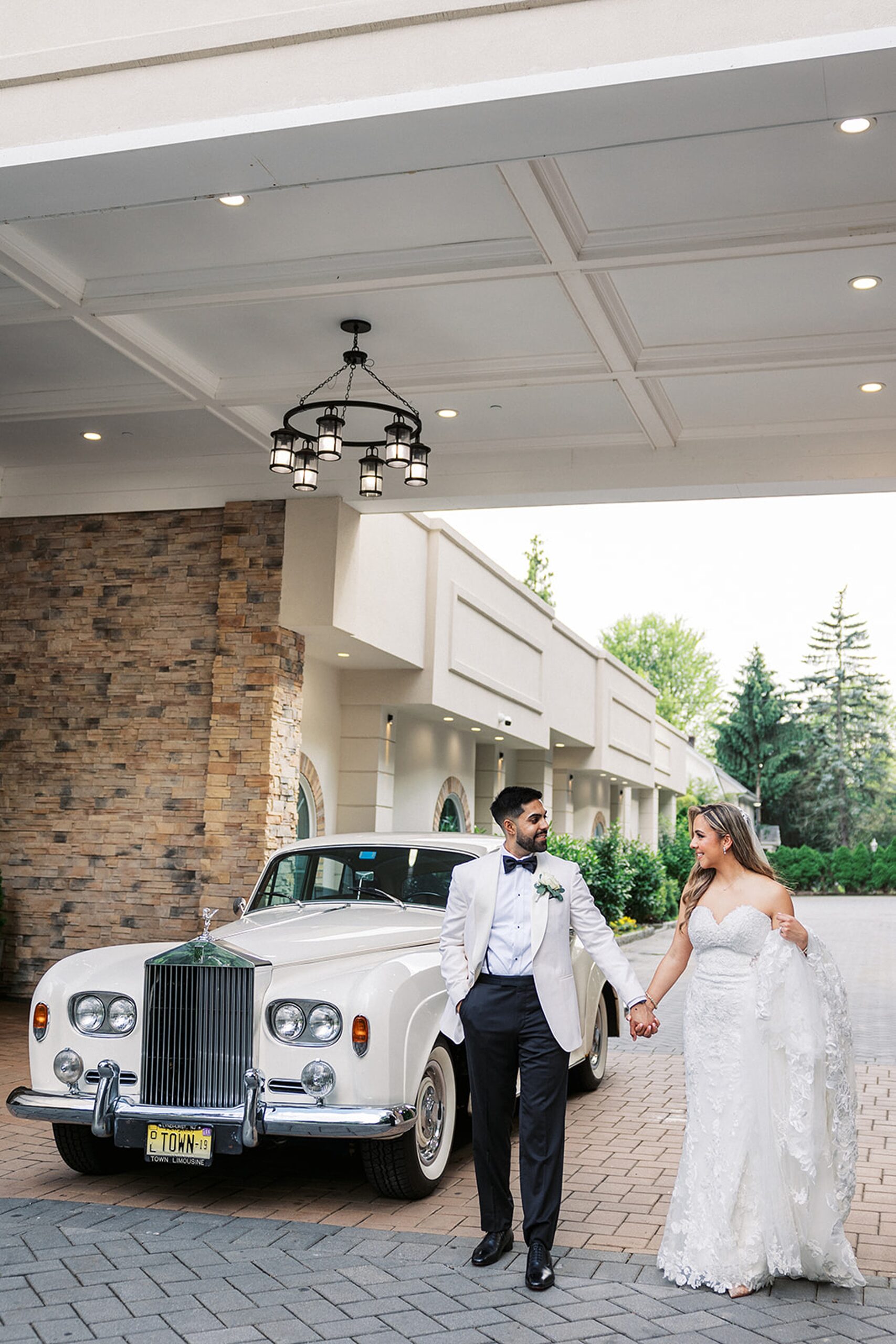 Newlyweds walk hand in hand by an antique limo under a car port at a valley regency wedding