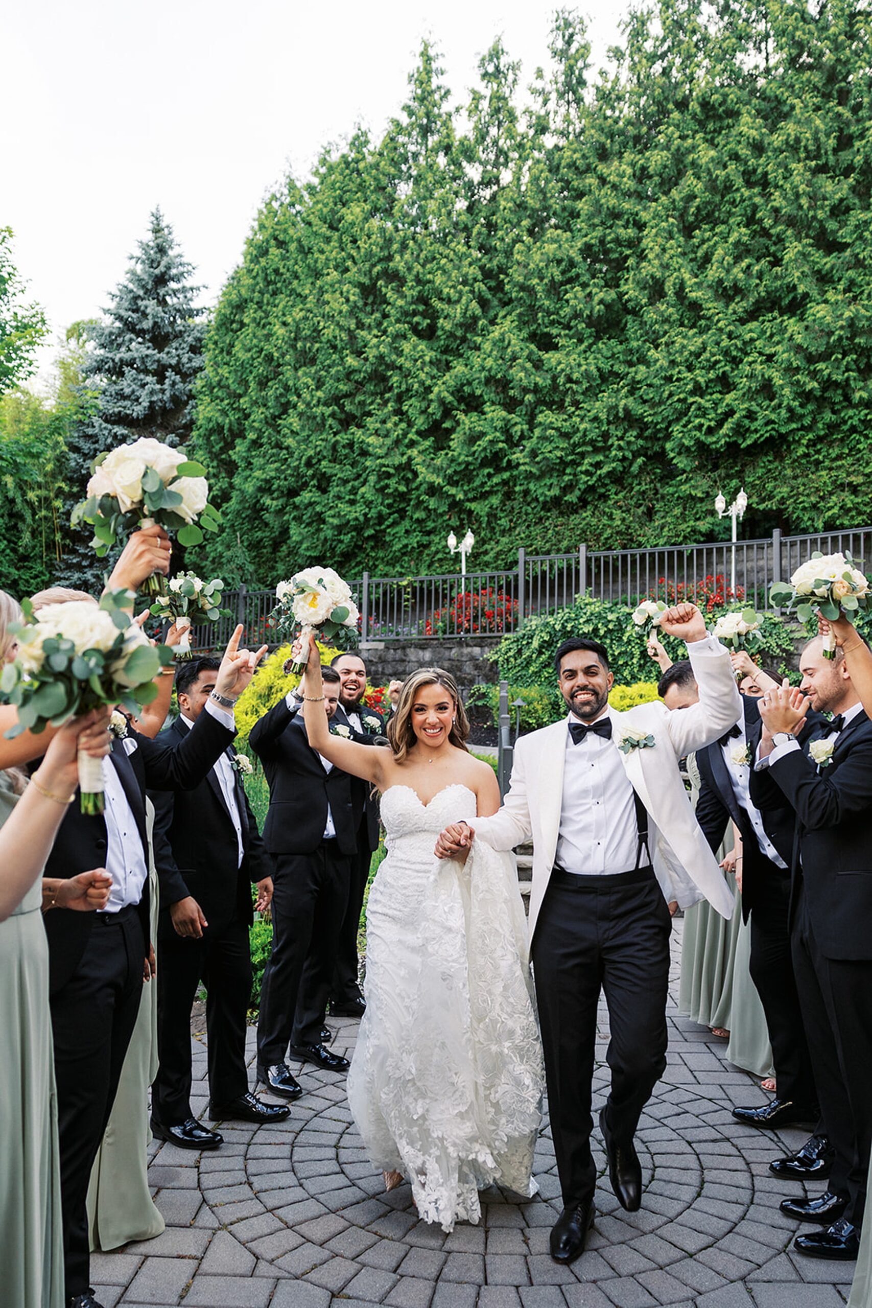 Newlyweds walk through an aisle formed by their wedding party as they all celebrate and cheer