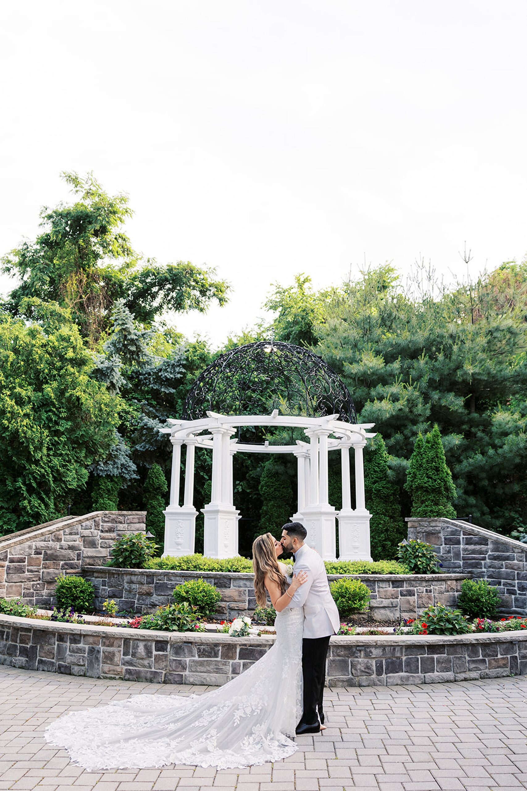 Newlyweds kiss in a garden in front of a raised white gazebo at a valley regency wedding