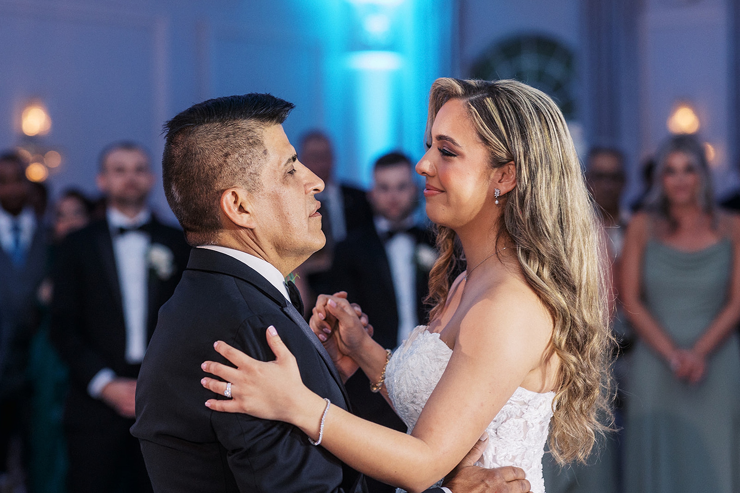 A bride dances with her father while her guests watch around the dance floor
