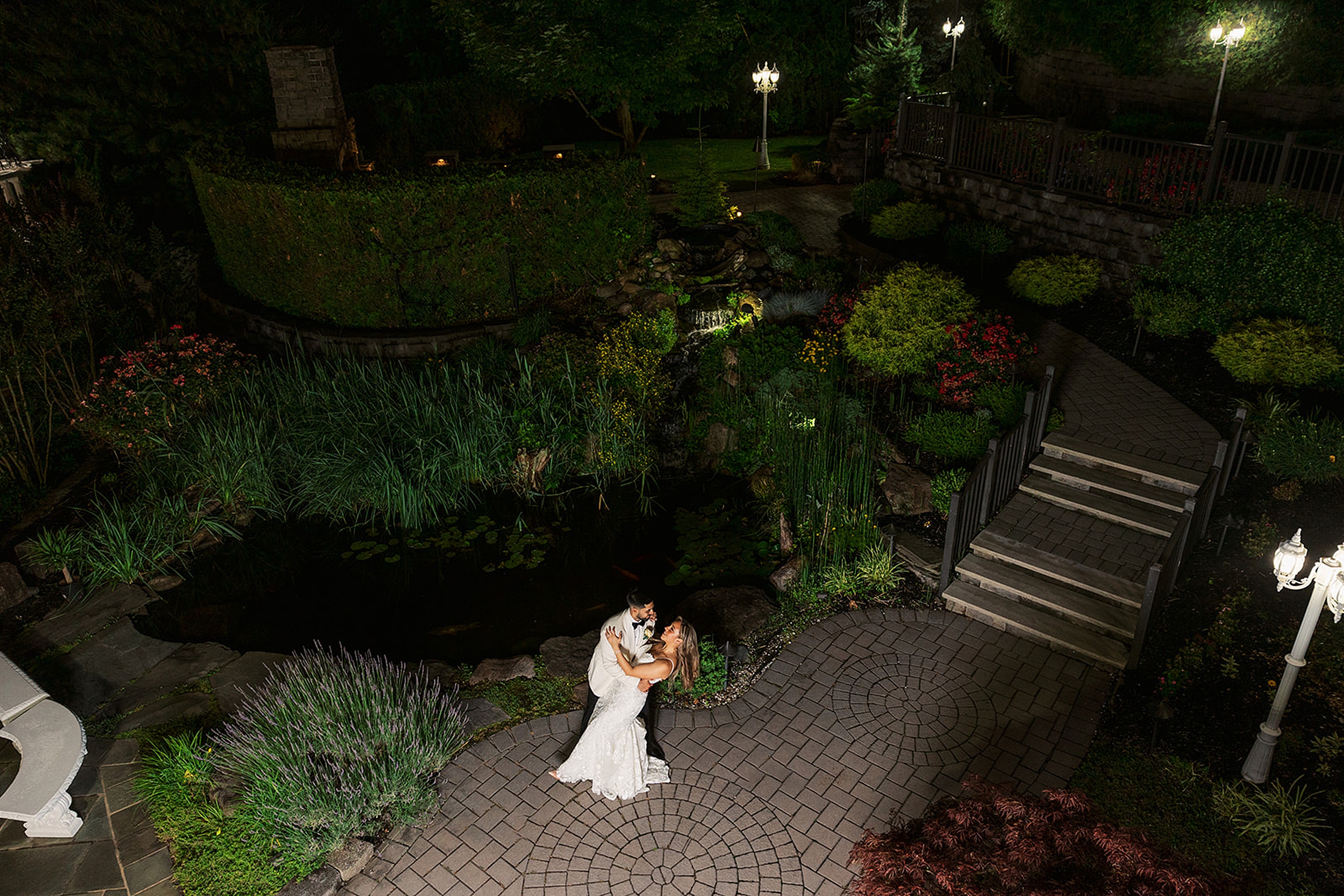 Newlyweds dance in a garden path by a pond at night at their valley regency wedding