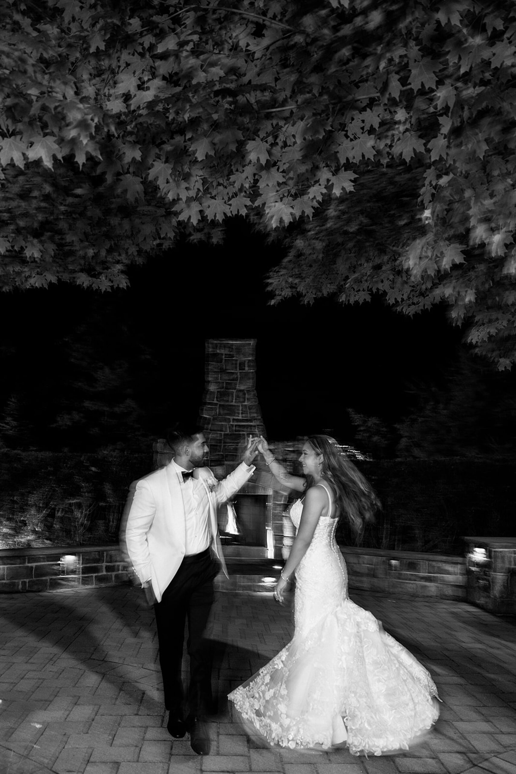 Newlyweds dance under a maple tree on a stone paved patio with a brick oven