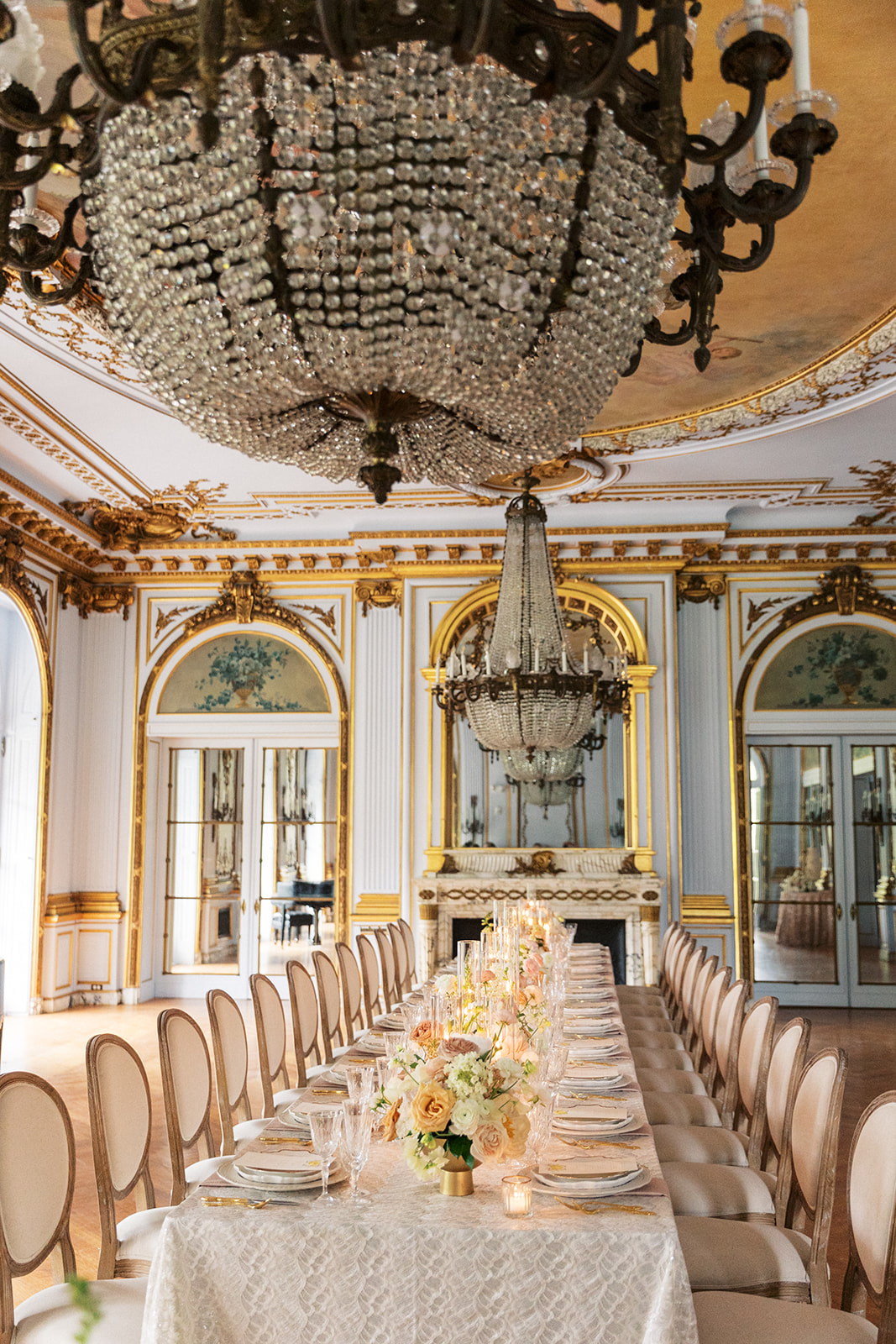 Details of a wedding reception table set up with ornate chairs and large chandeliers in a gold trim room at the Elkins Estate