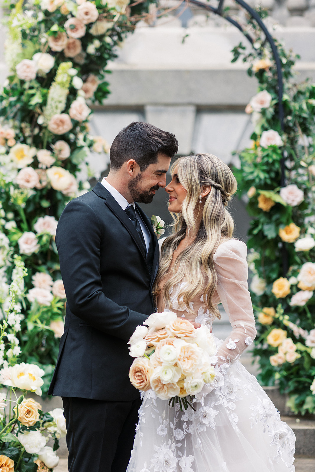 Newlyweds lean in for a kiss under a flower arch of white and pink roses
