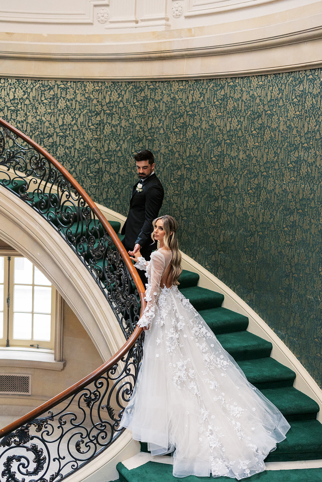 Newlyweds walk up a grand staircase with green carpet in the Elkins Estate