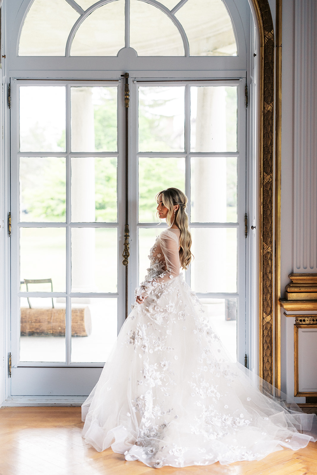 A bride in a lace dress stands in a large french door in the getting ready room of the Elkins Estate