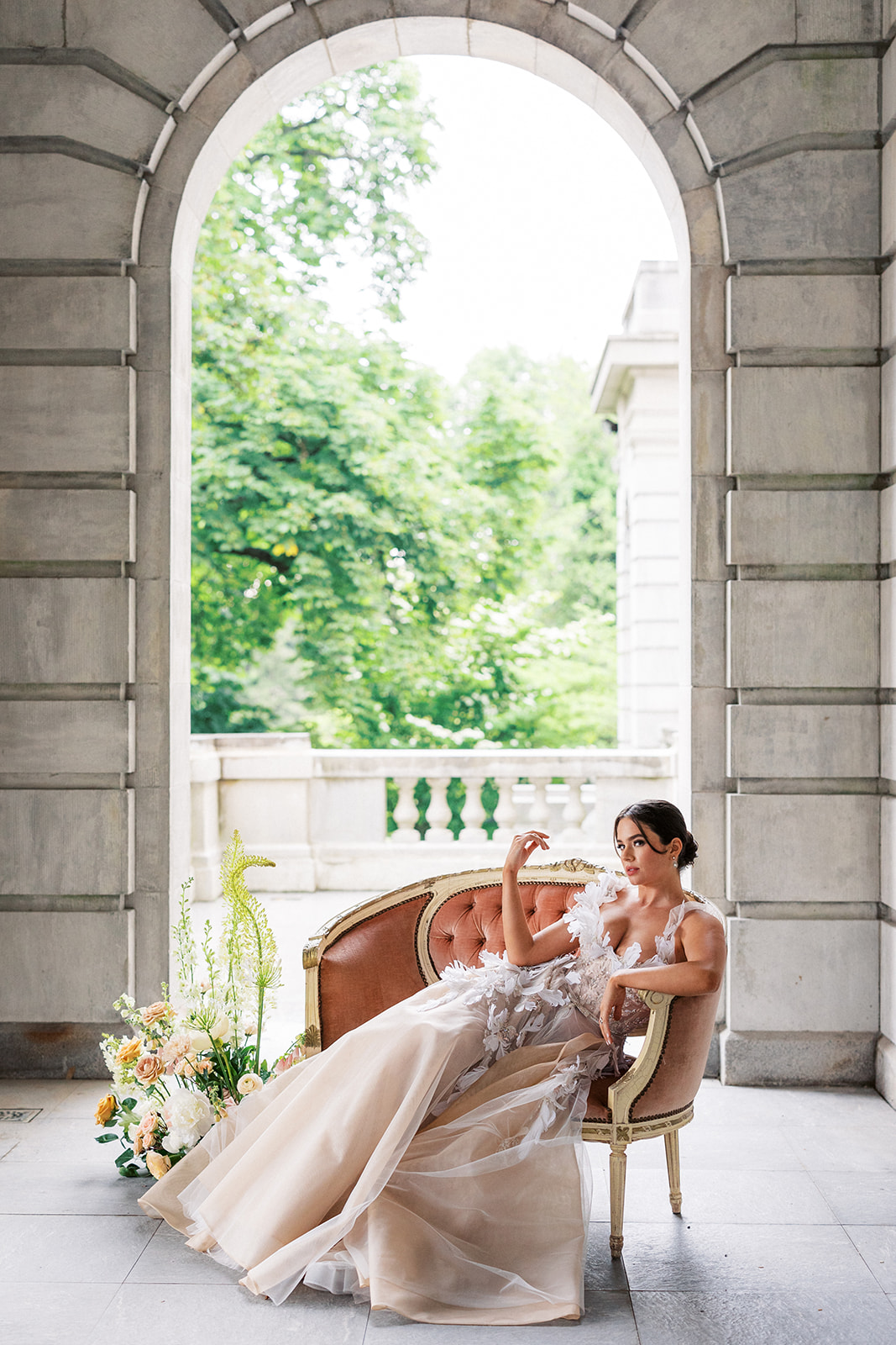 A bride lounges on a pink antique couch under an arch on a patio of the luxurious Elkins Estate