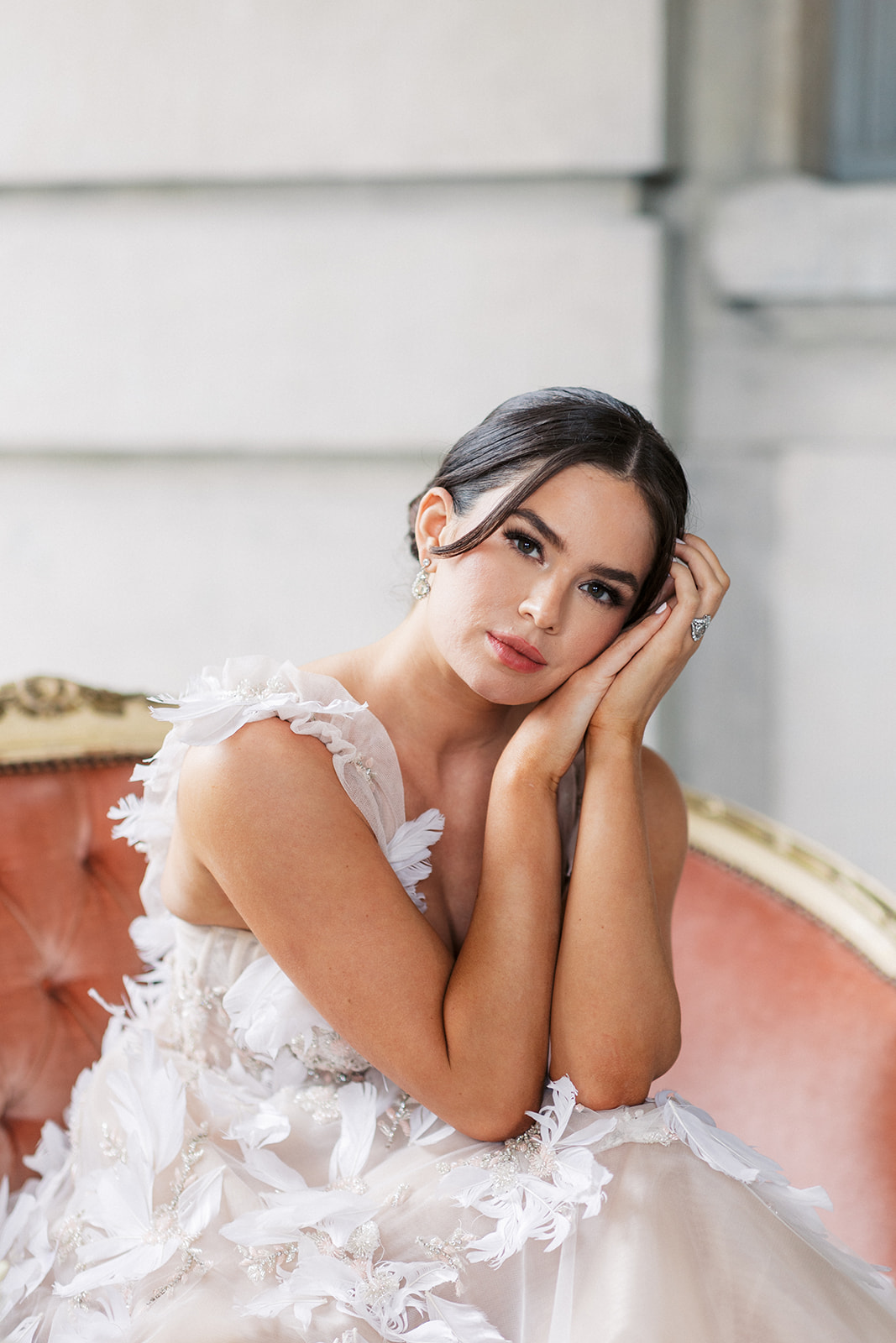 A bride rests her head on her hands while sitting on a pink antique couch outside