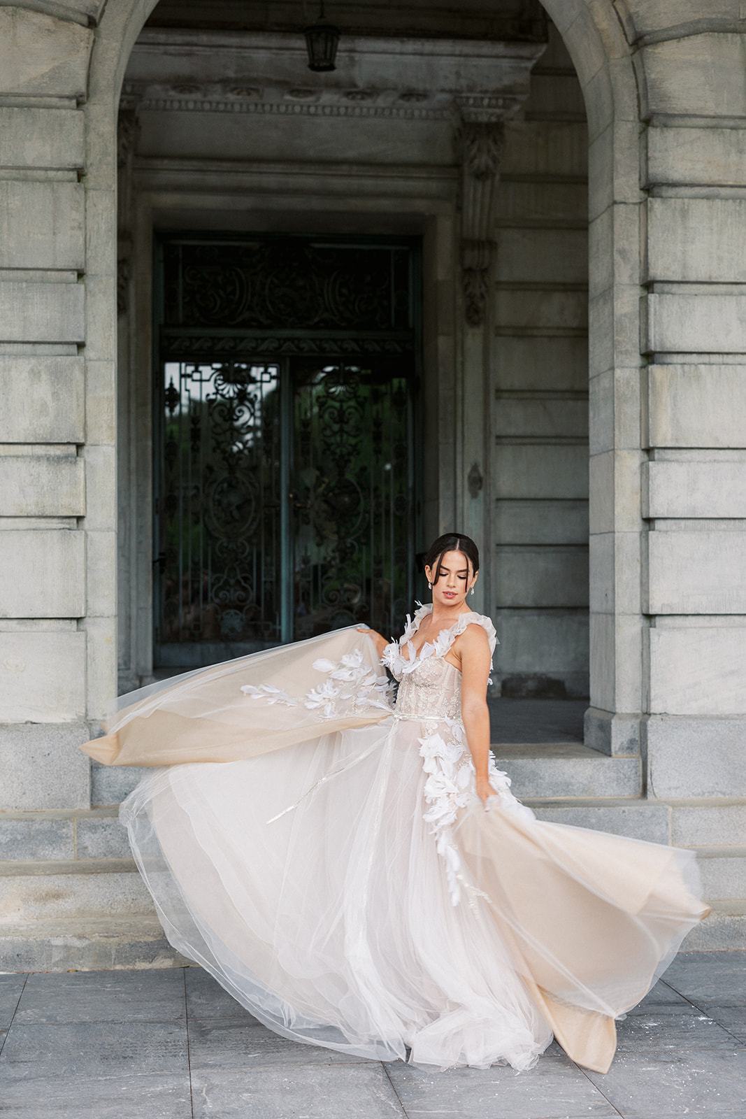 A bride twirls her dress and dances at the entrance and iron doors of the Elkins Estate