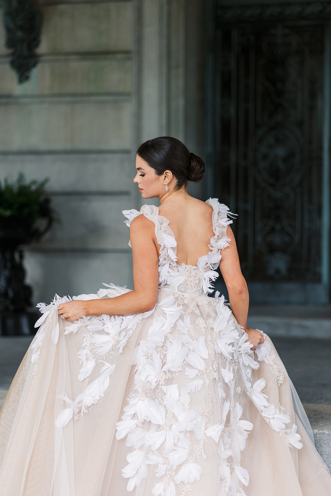 A bride holds her dress while walking up the steps to the large doors of her wedding venue