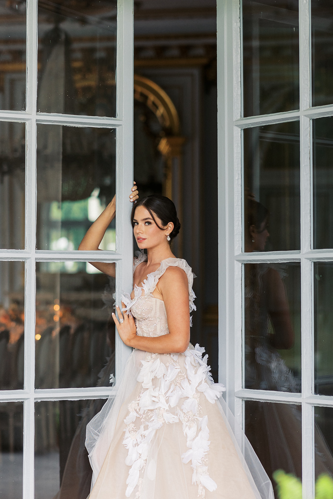 A bride stands in a large glass door leaning on it at the Elkins Estate