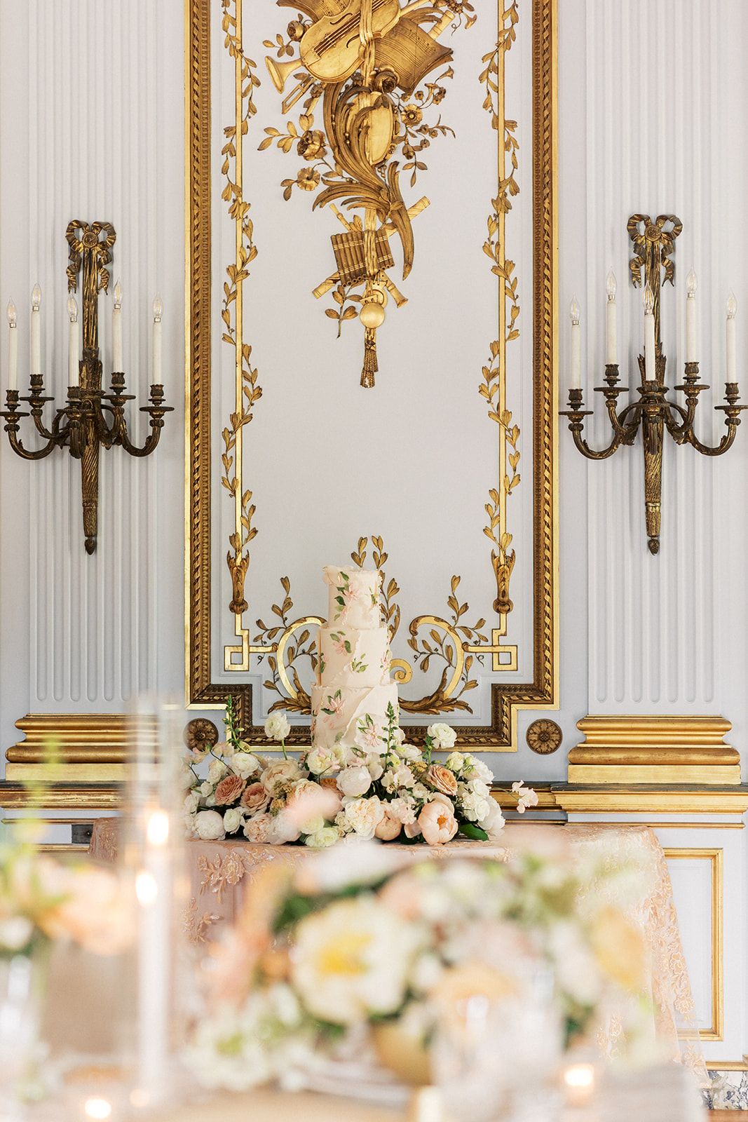 Details of a cake sitting under ornate gold decor and wall sconces
