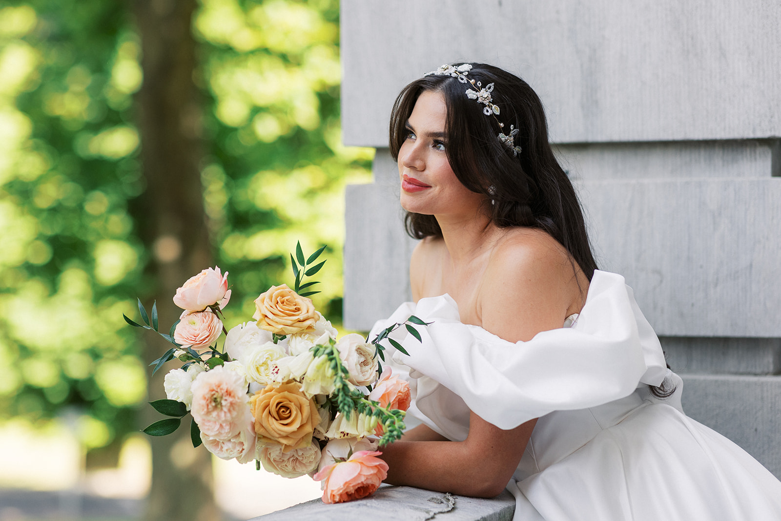 A bride leans on a railing looking out to a garden holding a large bouquet