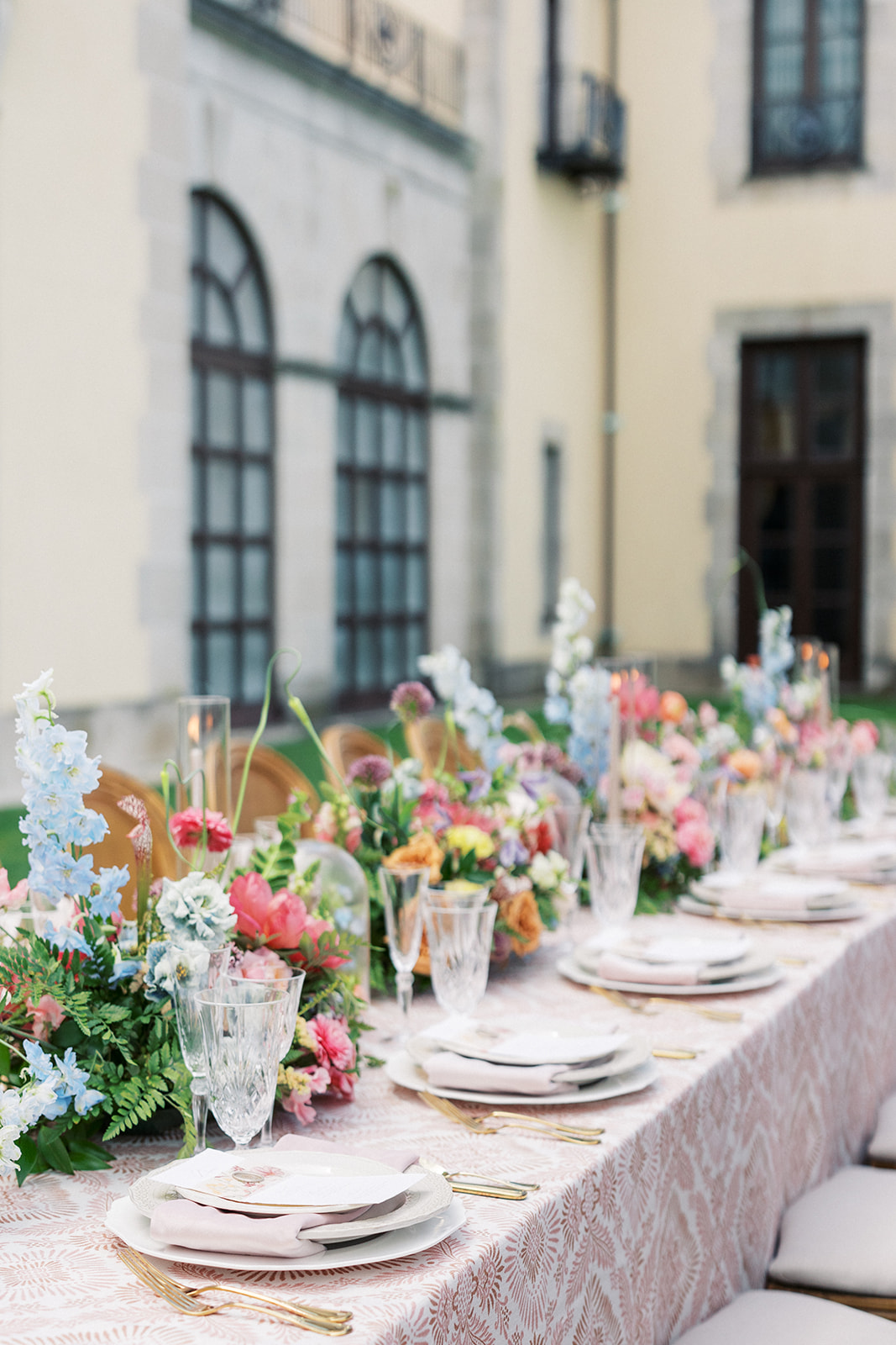 Details of a wedding reception set up outside with gold silverware and colorful florals at the Oheka Castle
