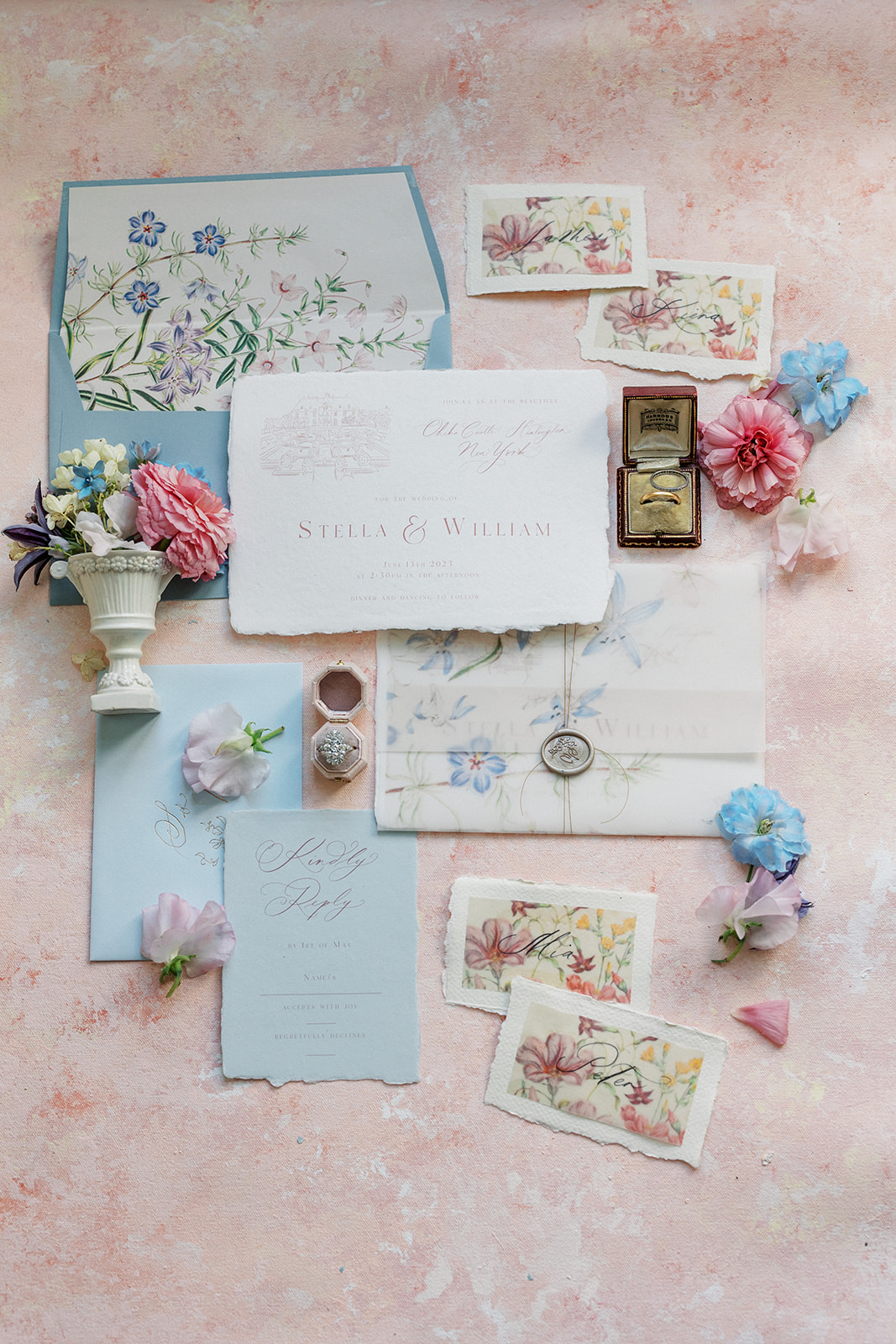 Details of a wedding invitation, rings, flowers and save the date sit on a pink table