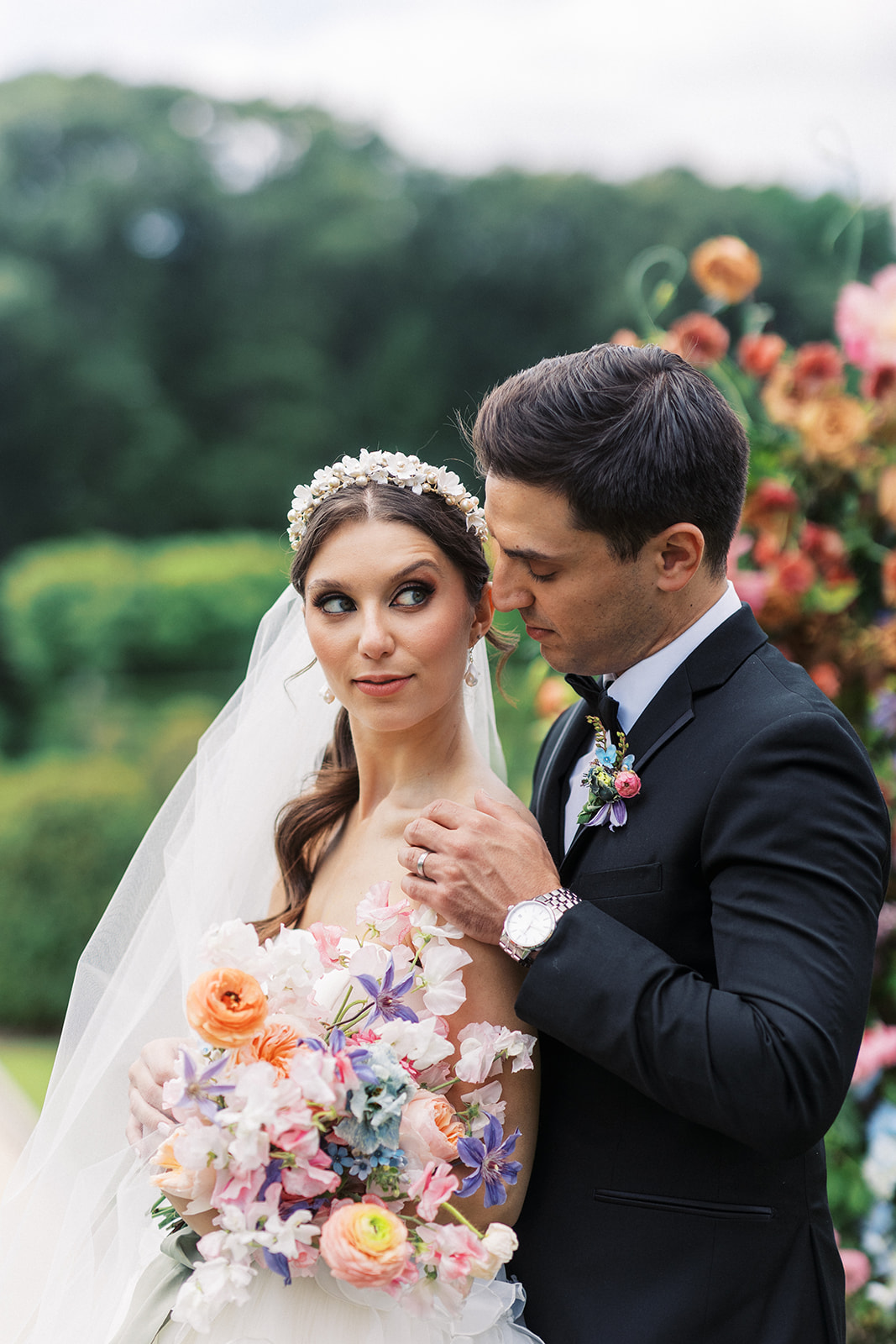 Newlyweds stand in a garden in a black tuxedo and long veil