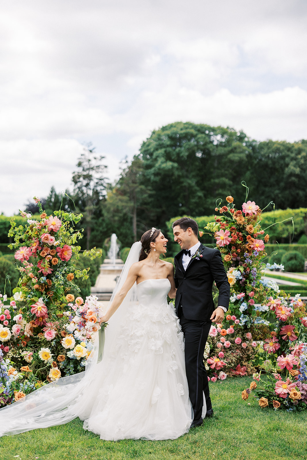 Newlyweds laugh and walk through a large floral arch at their Oheka Castle wedding ceremony
