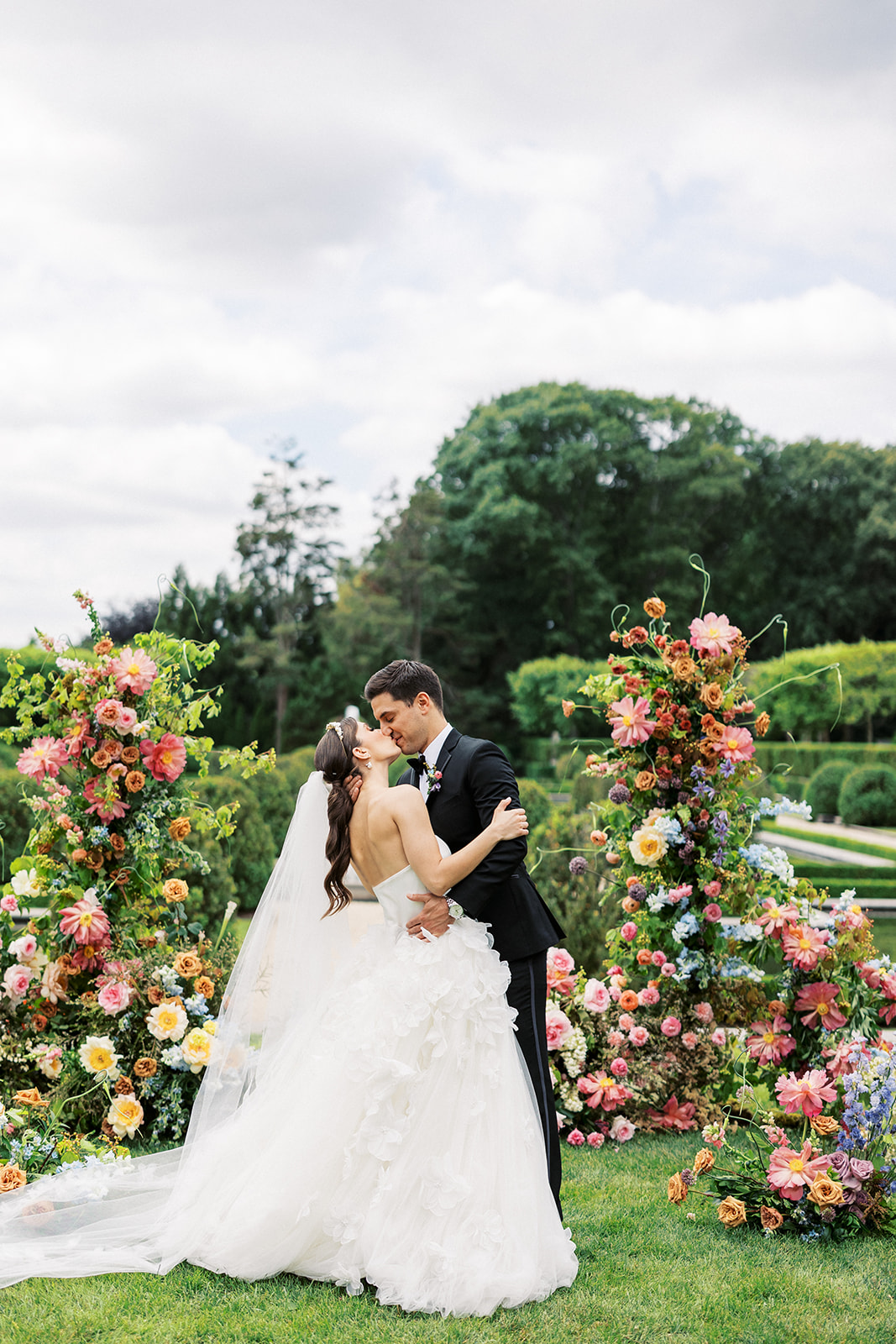 Newlyweds kiss among a large display of colorful florals during a wedding ceremony