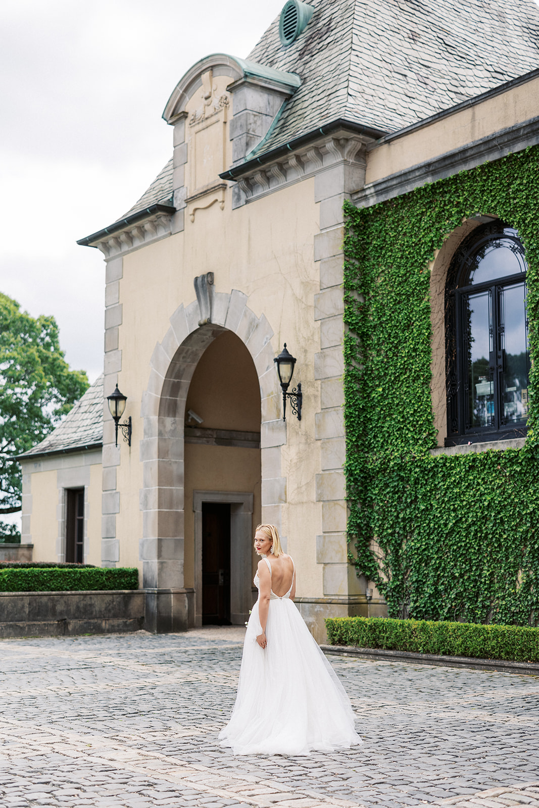 A bride looks over her shoulder while walking in the gravel patio of the Oheka Castle