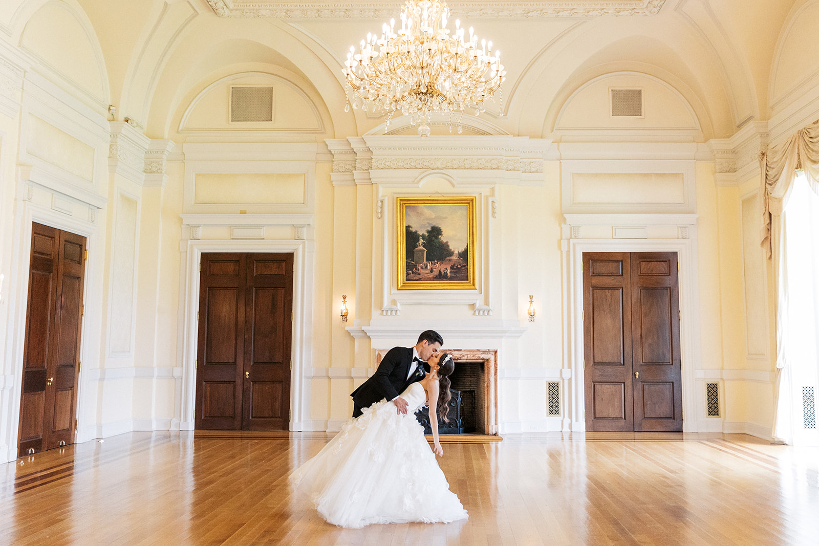 Newlyweds dip and kiss under a large chandelier in the Oheka Castle