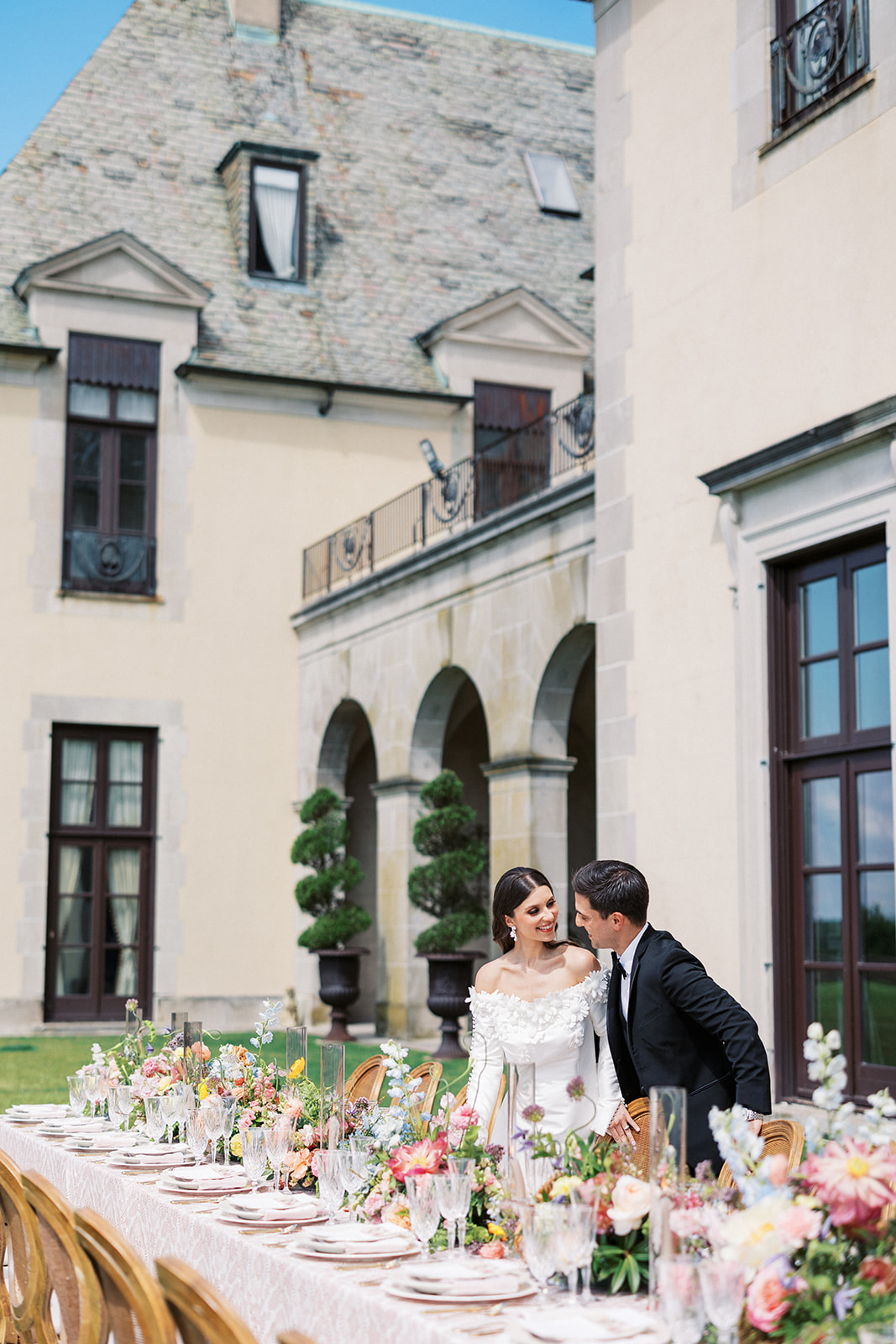 Newlyweds gaze at each other while standing over a colorful outdoor reception table at an Oheka Castle wedding