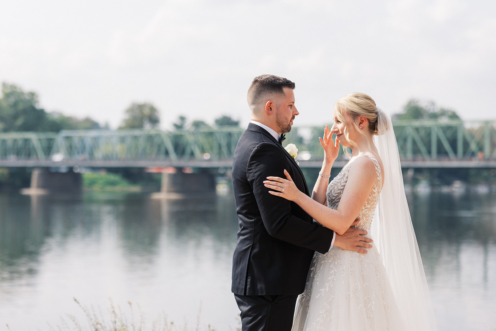 A bride wipes away tear as she stands with her groom on a river bank during their Lambertville Station Wedding first look