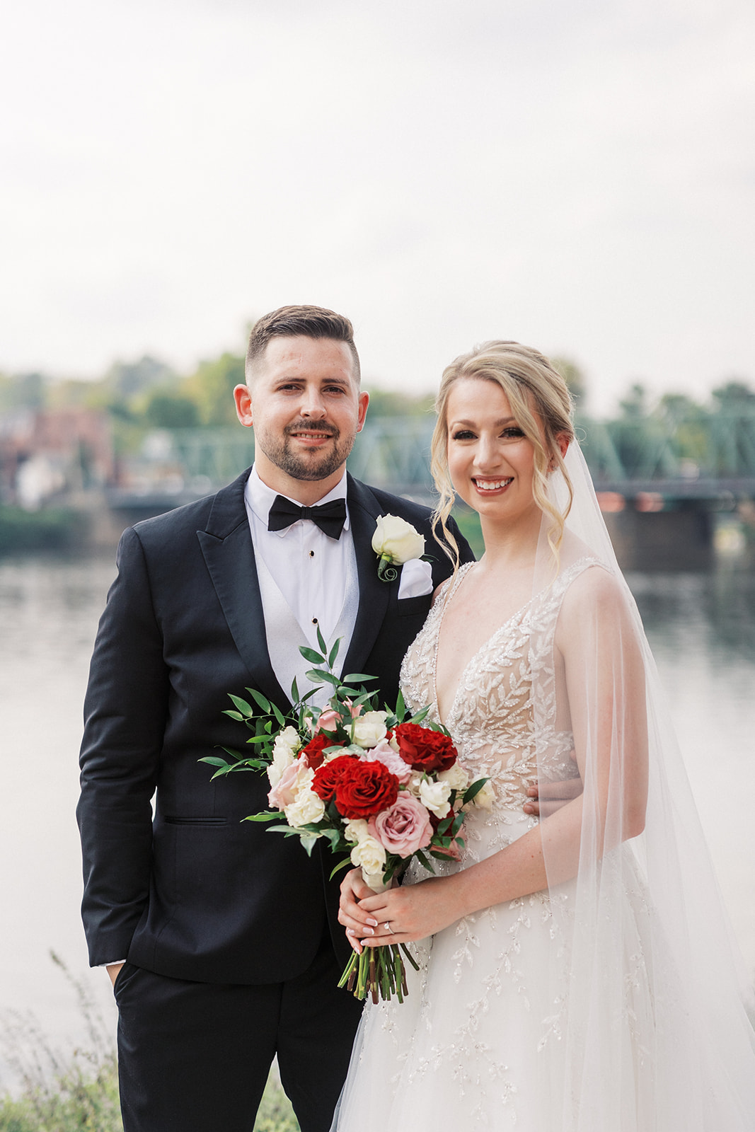 Newlyweds stand together smiling in a riverfront garden