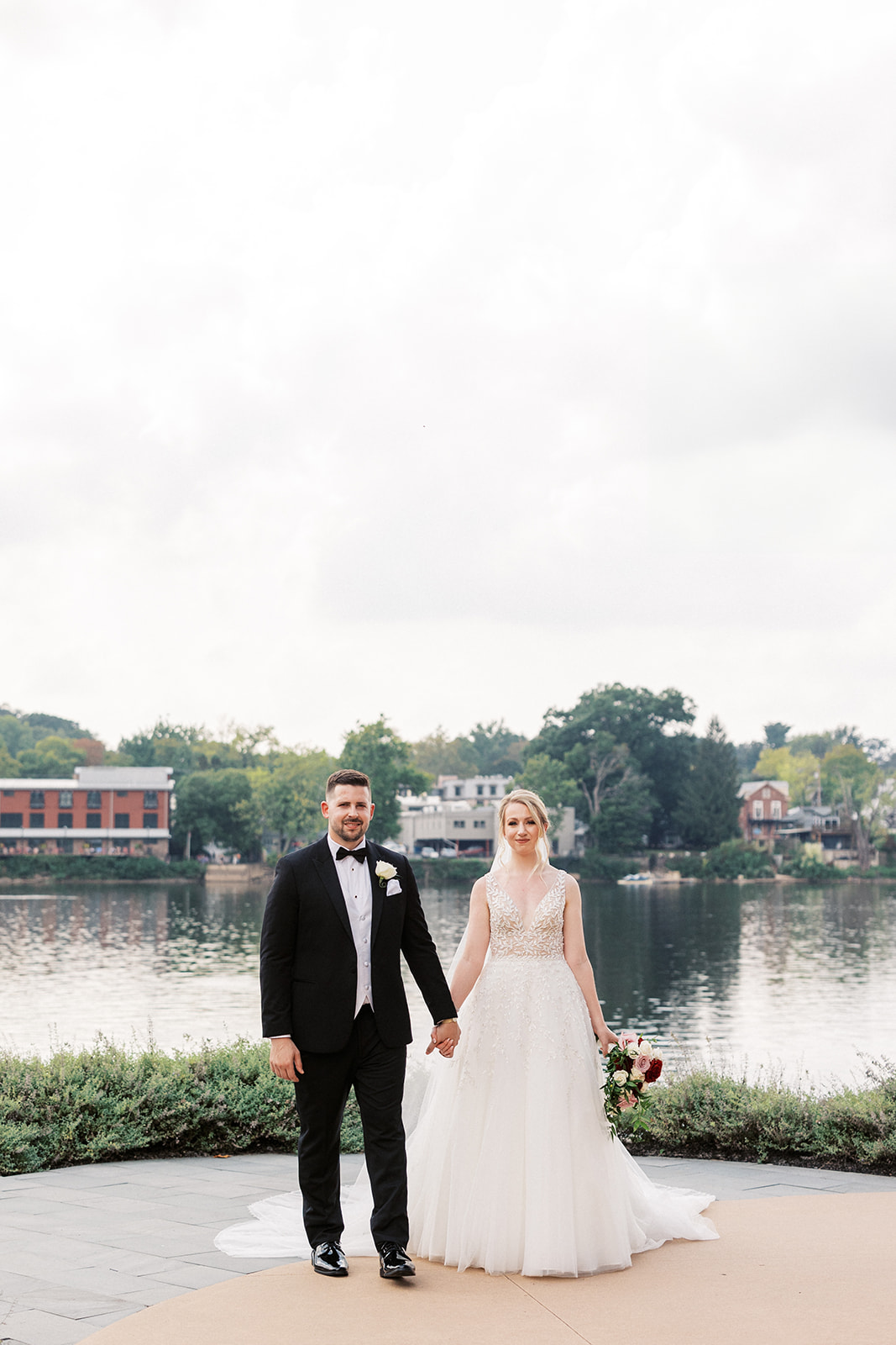 Newlyweds hold hands while walking through a riverfront garden patio