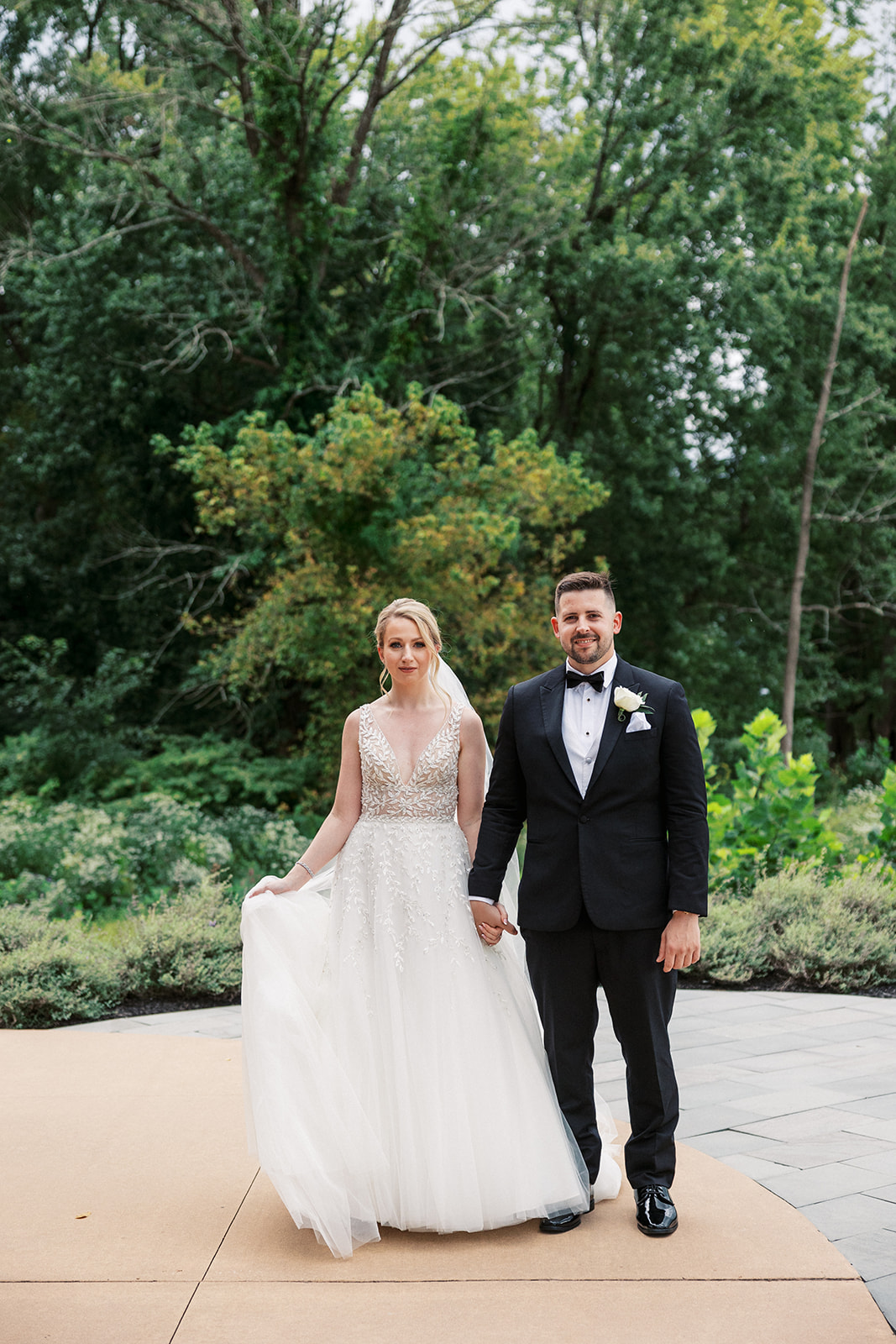 Newlyweds hold hands and walk through a garden patio at a Lambertville Station Wedding