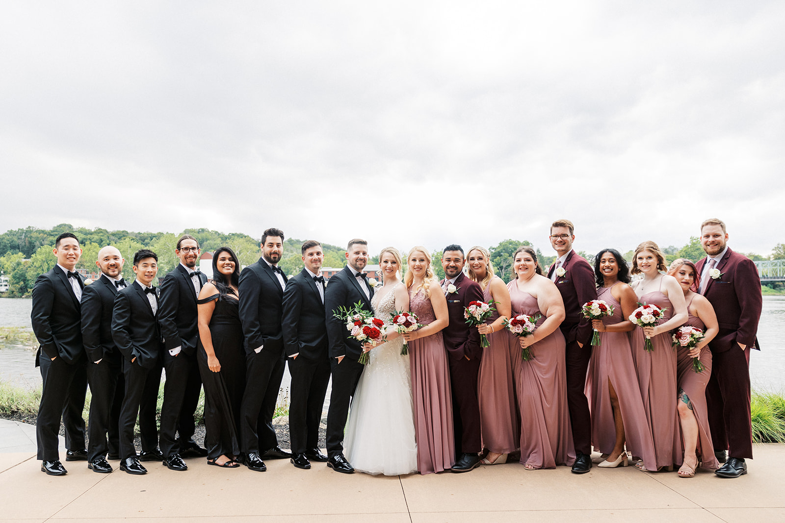 Newlyweds stand together with their large bridal party on a riverfront patio at a Lambertville Station Wedding