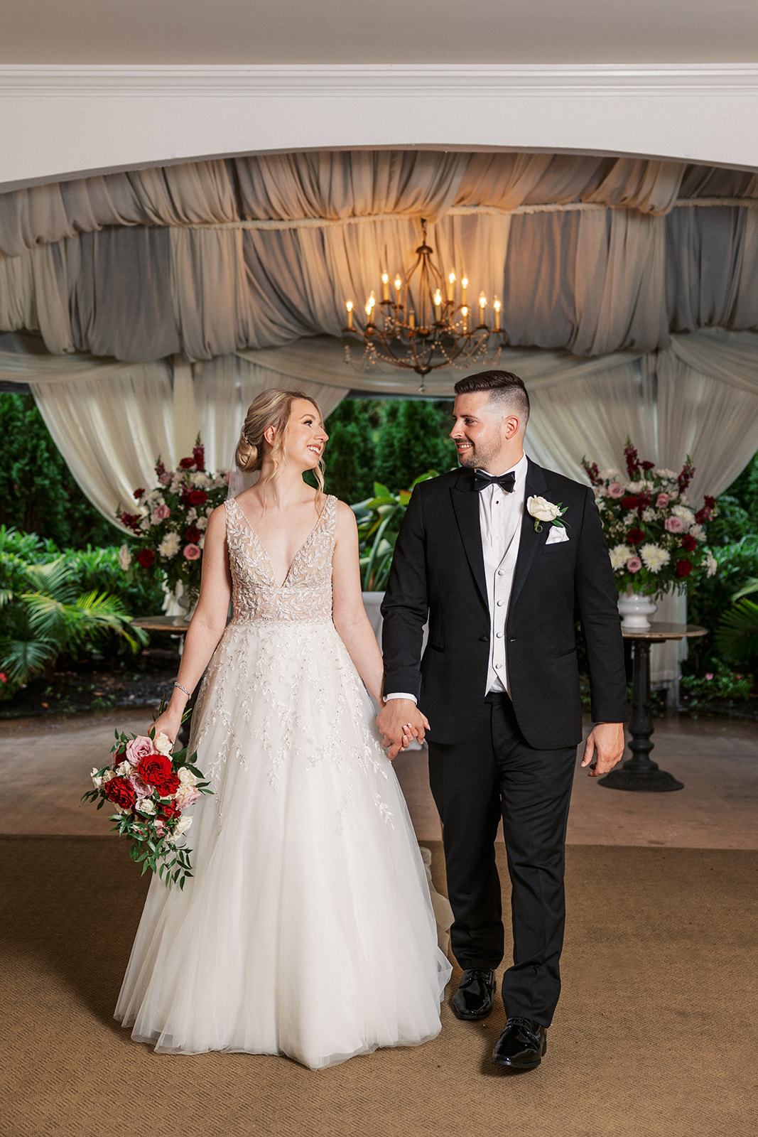 Newlyweds hold hands while walking under a chandelier and looking at each other at Lambertville Station Wedding