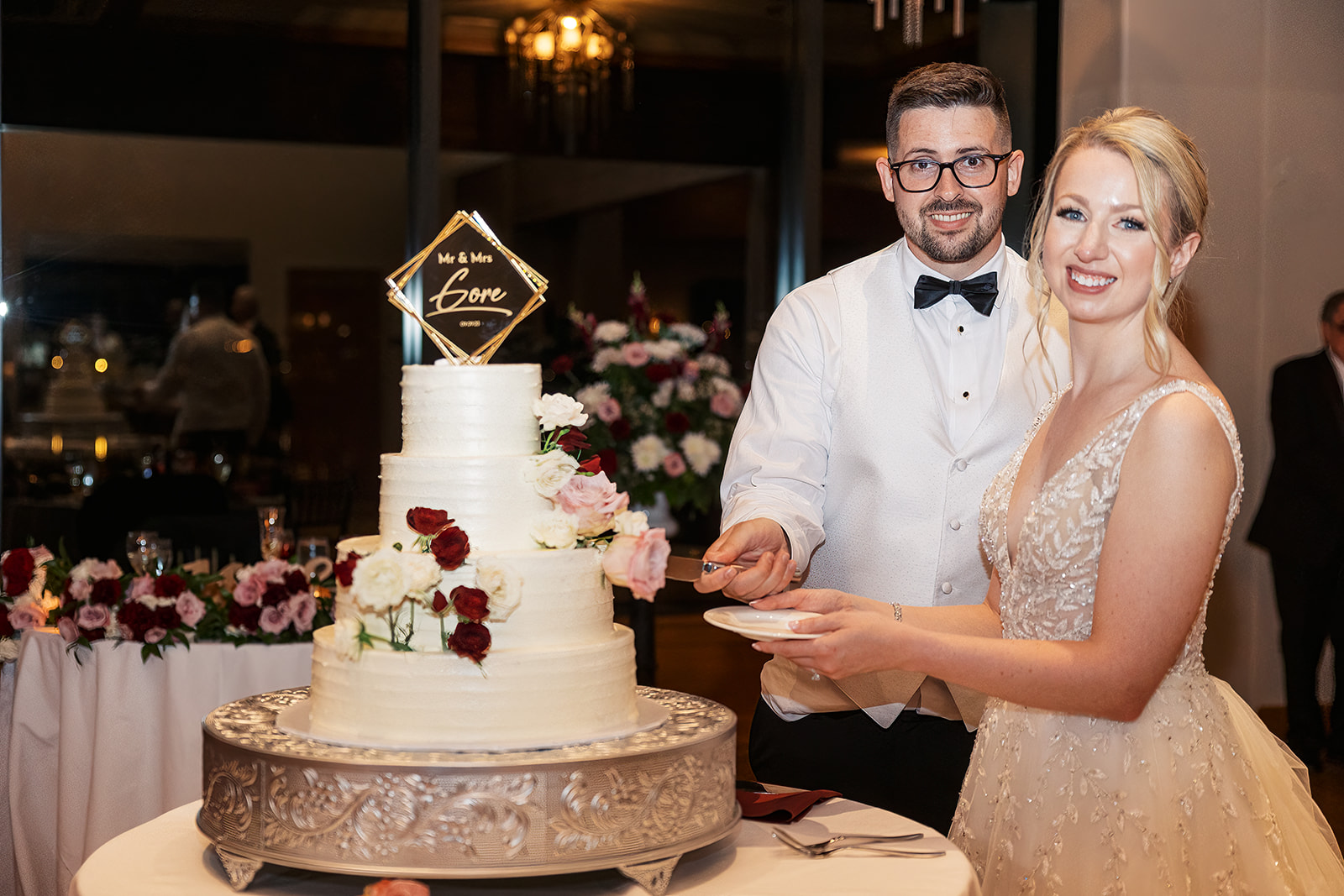 Newlyweds cut the three tier cake together decorated with roses and a custom gold topper