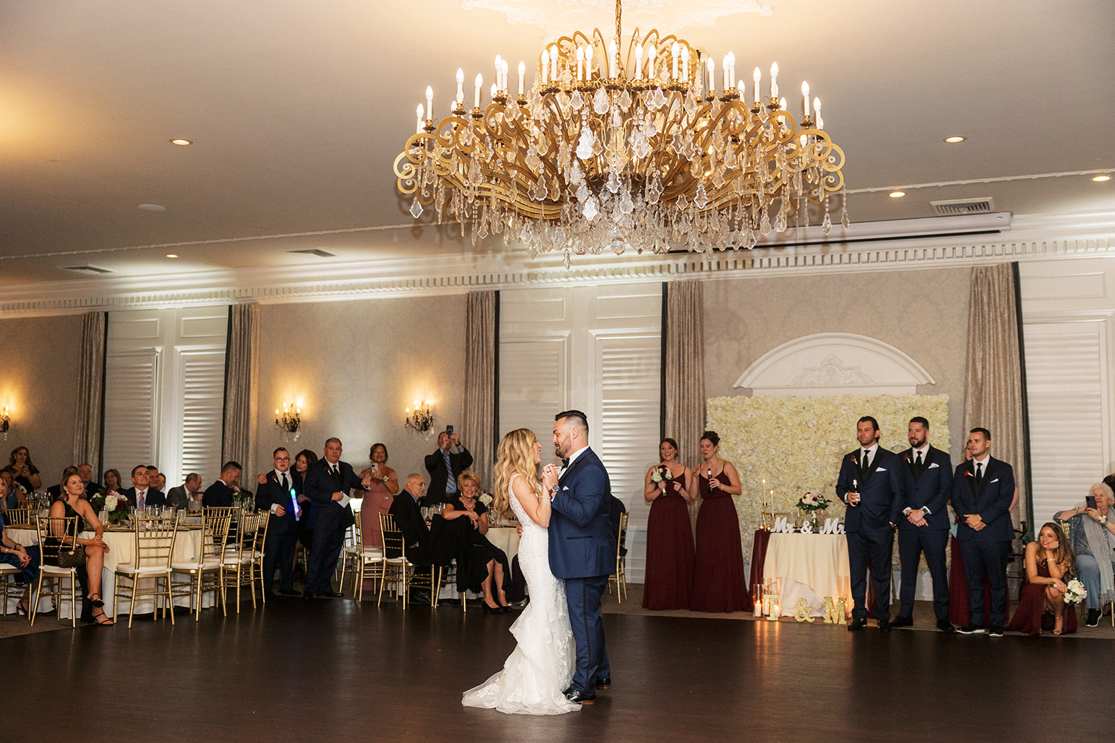 Newlyweds dance under a large chandelier surrounded by guests watching at the The Belle of Blue Bell reception venue