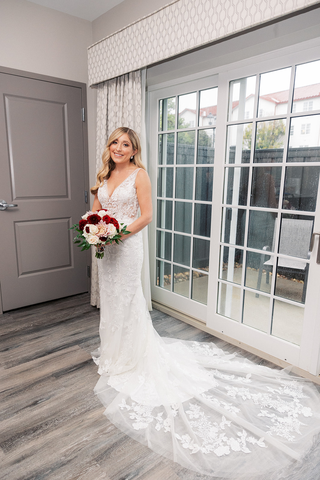 A bride smiles while standing in a getting ready room by a porch