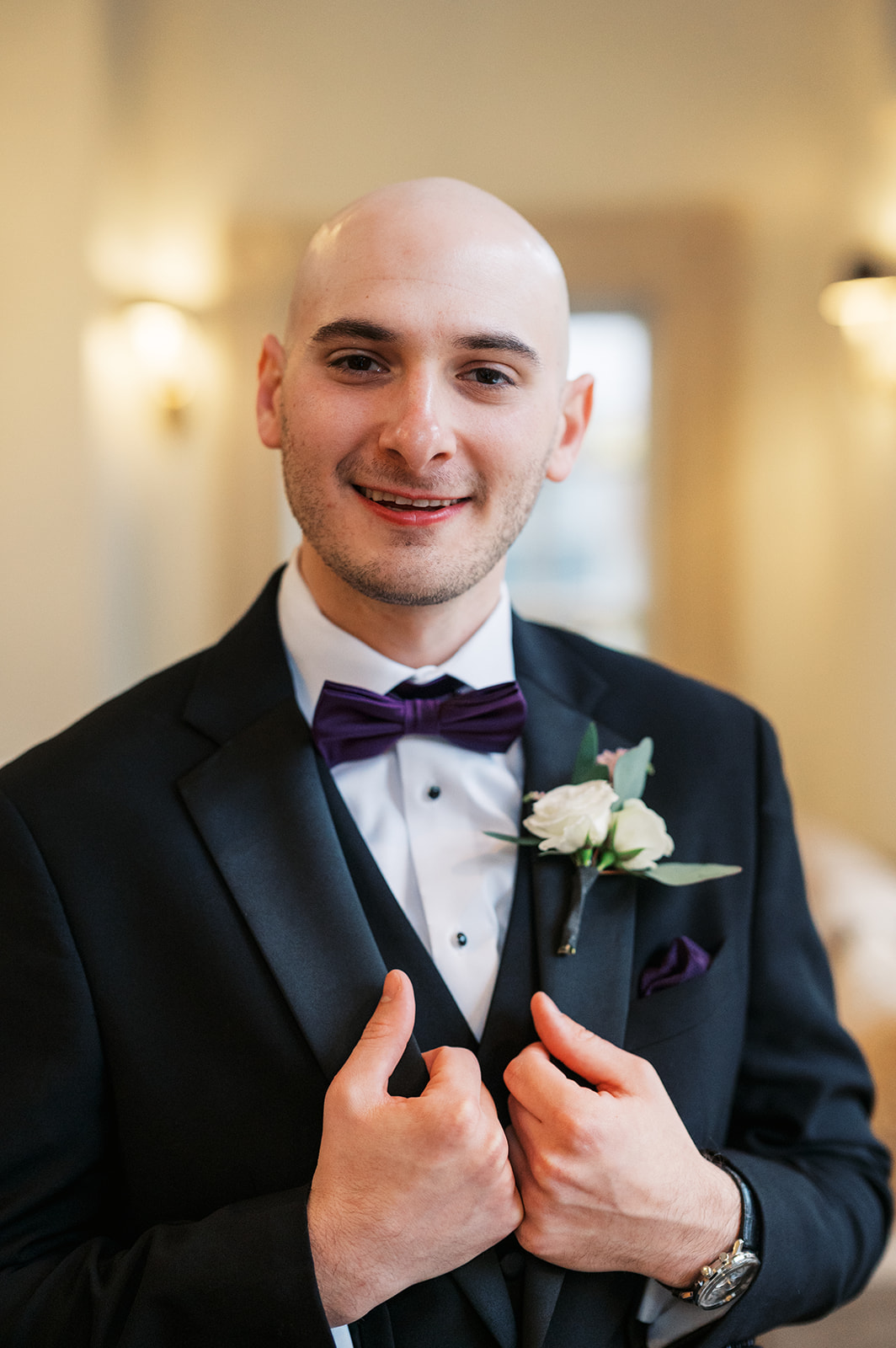 A groom smiles and holds his lapels while getting ready for his wedding
