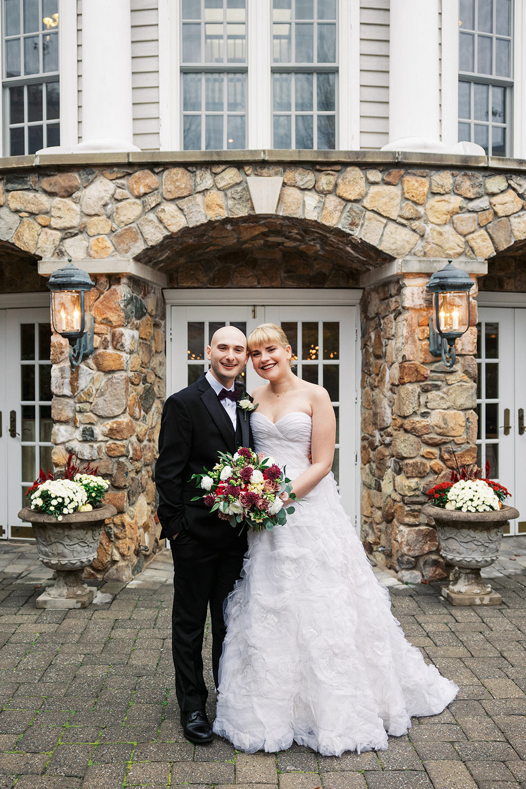 Newlyweds stand on a paved patio holding the colorful bouquet at an Olde Mill Inn Wedding