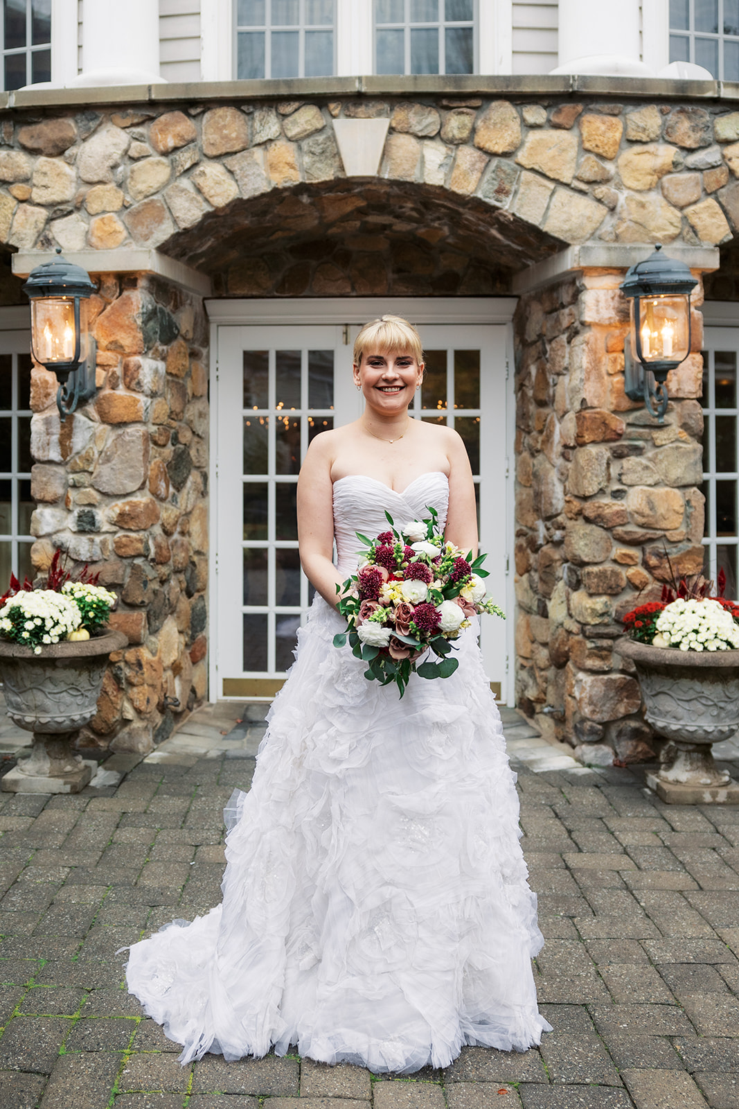 A bride holds her bouquet while standing outside the main stone entrance to her Olde Mill Inn Wedding