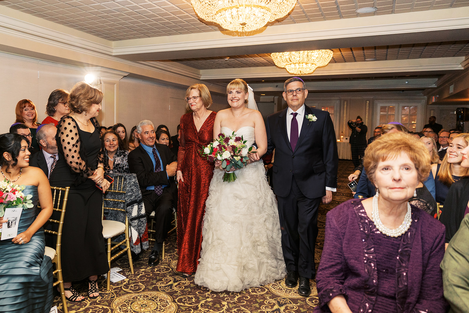 A bride walks down the aisle of her Olde Mill Inn Wedding escorted by mom and dad