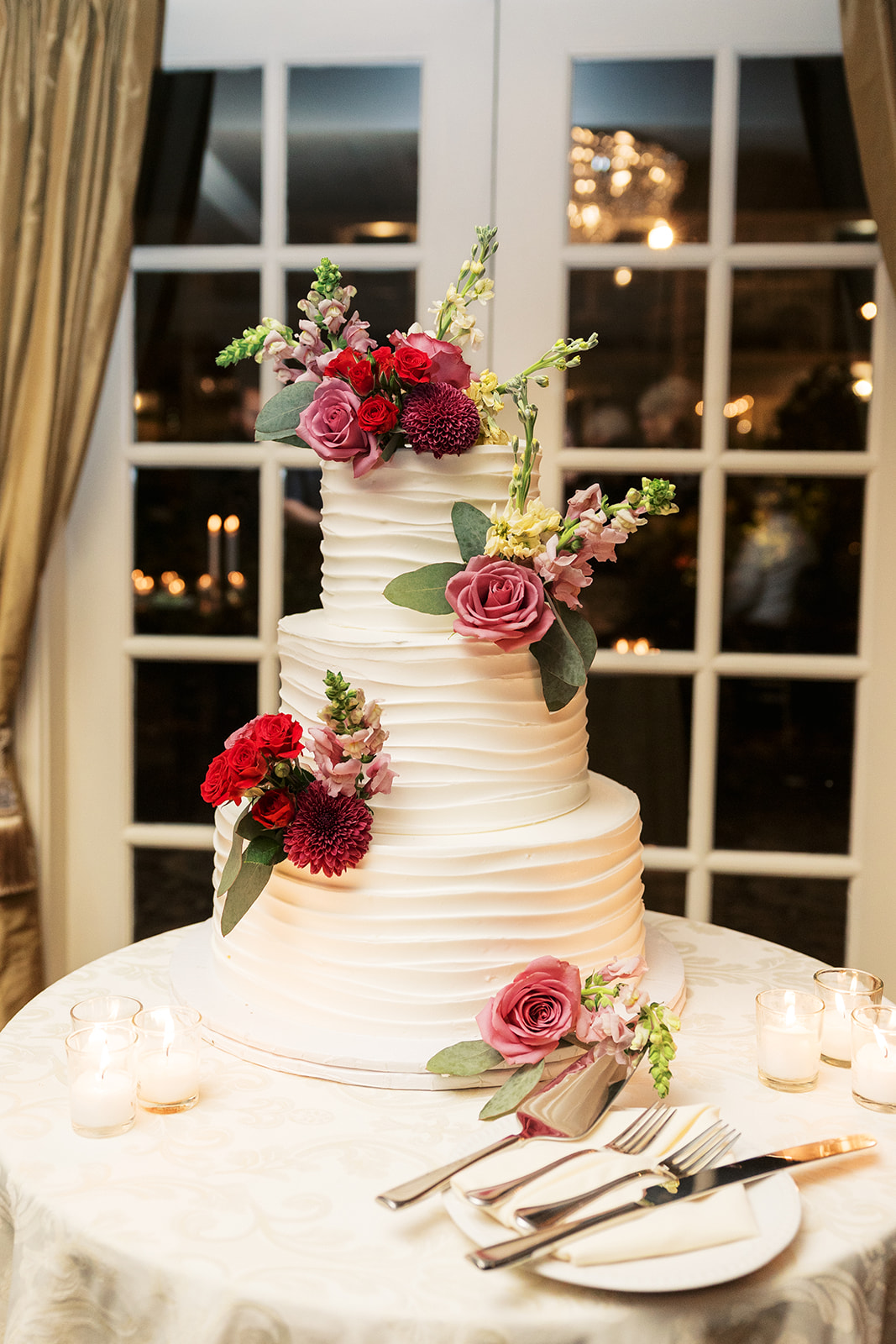 A three tier cake covered with red and pink flowers