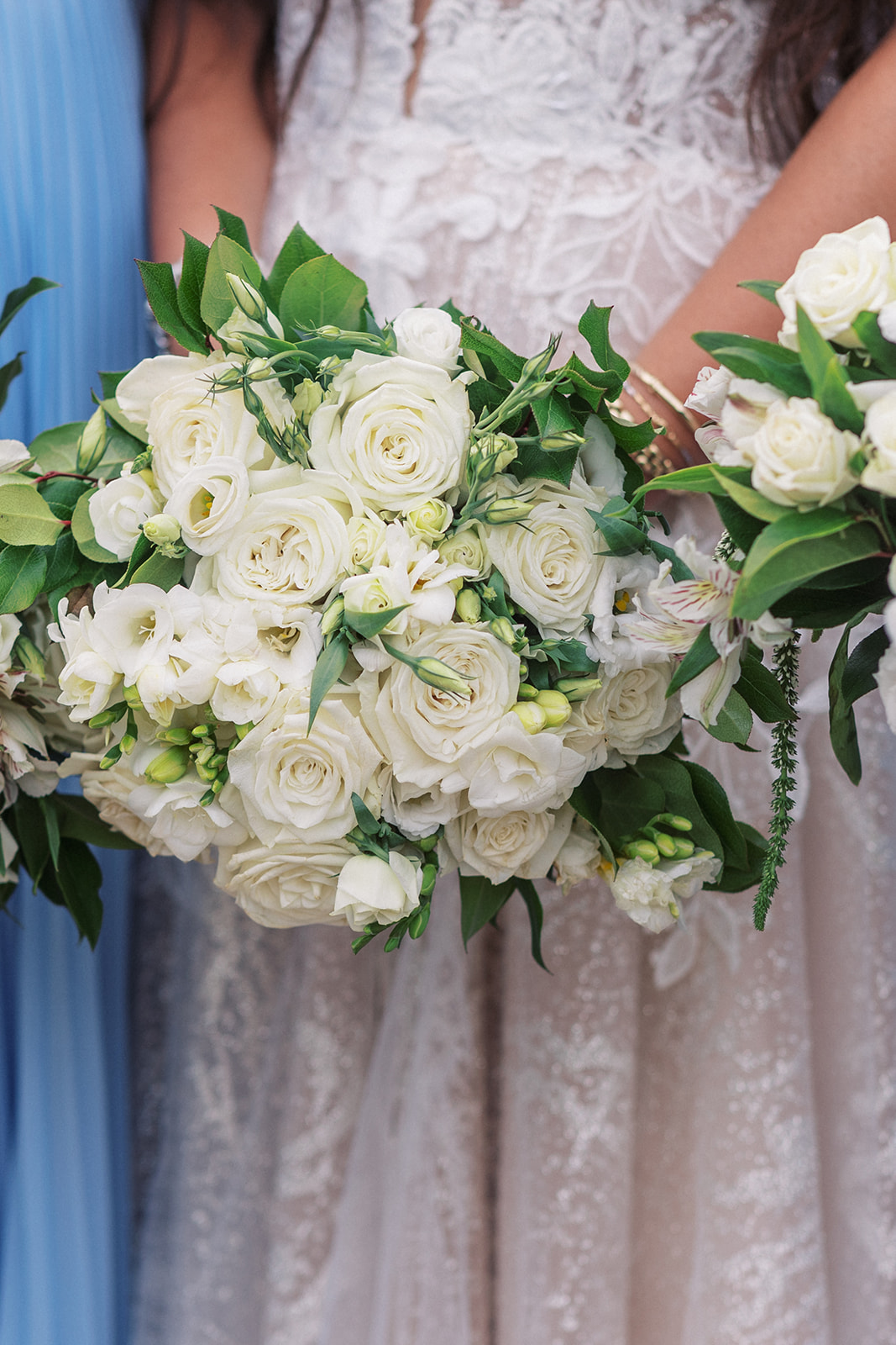 Details of a white rose bouquet held by a bride in a white lace dress
