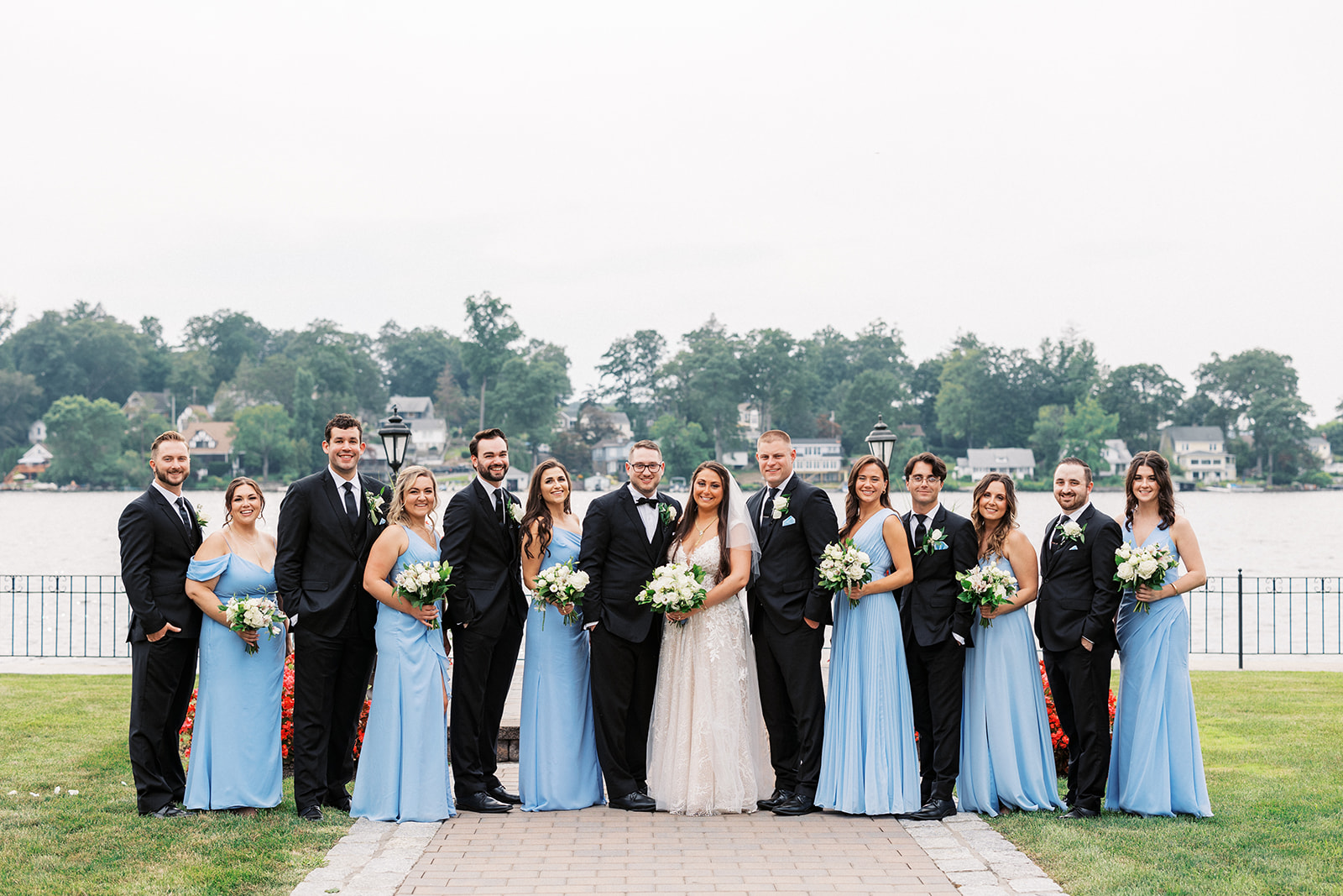 Newlyweds stand in a brick path with their entire bridal party in black and blue