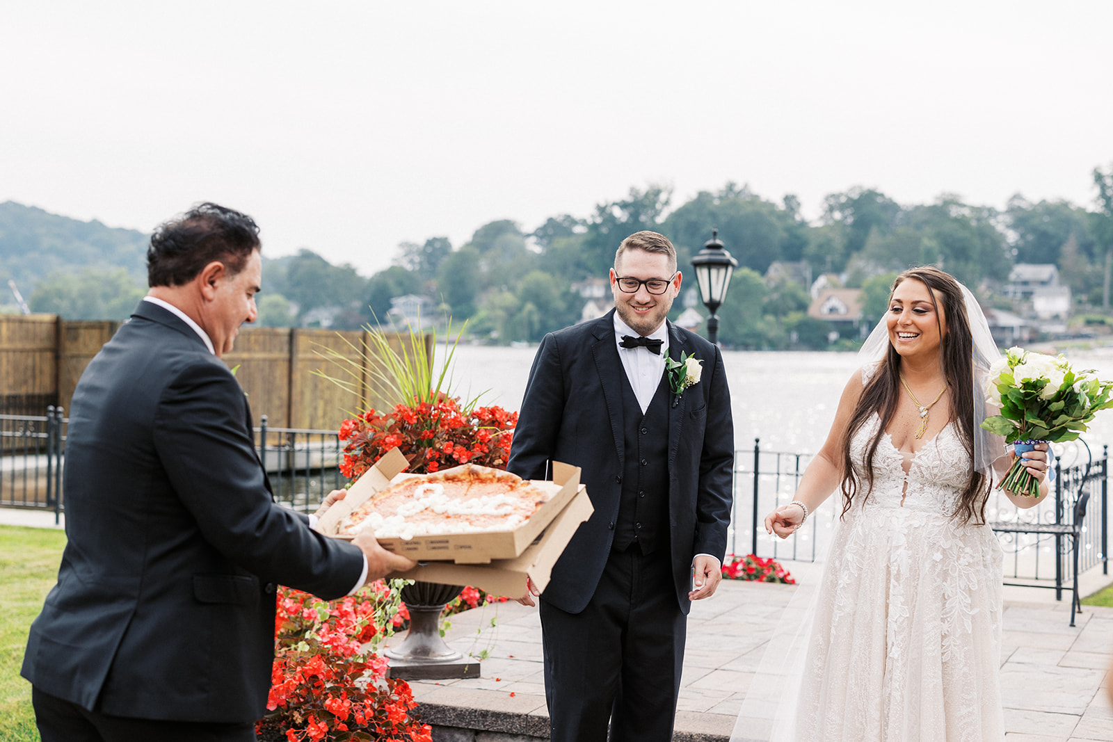 A dad in a black suit presents newlyweds with a pizza decorated