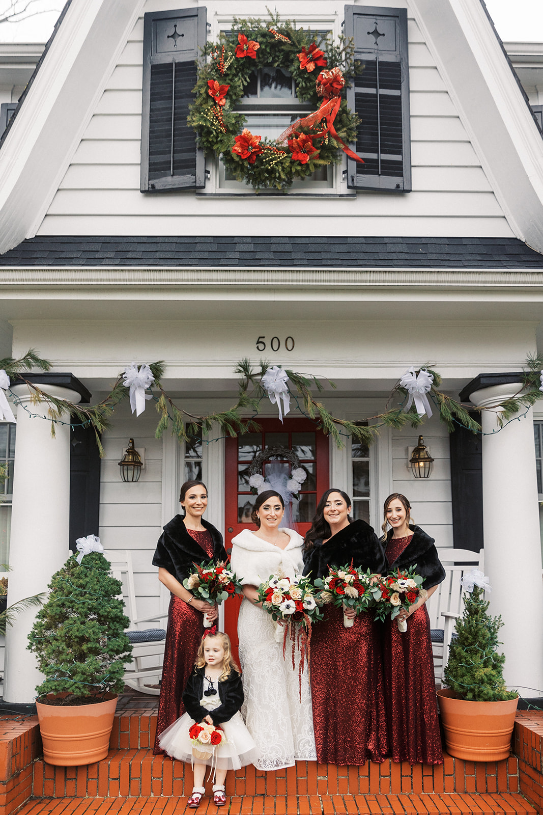 A bride stands on a stoop with her bridal party holding their bouquets at christmas time for her Above Weddings