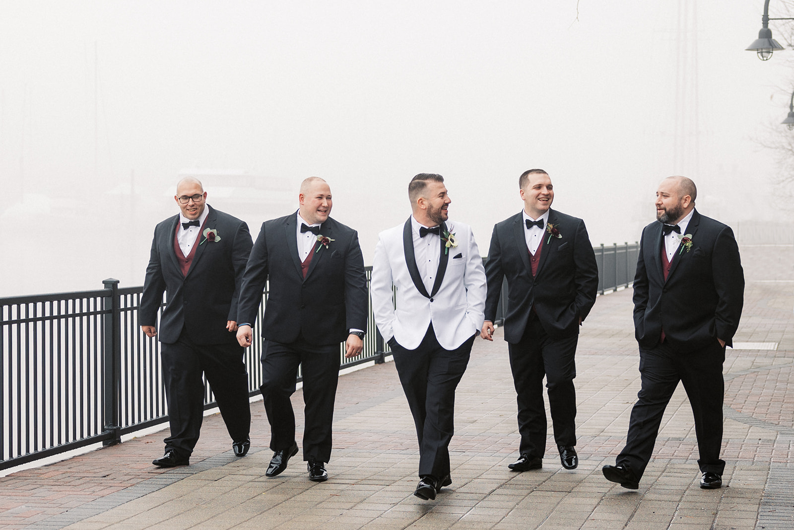 A groom walks through a riverside park with his groomsmen at his Above Weddings
